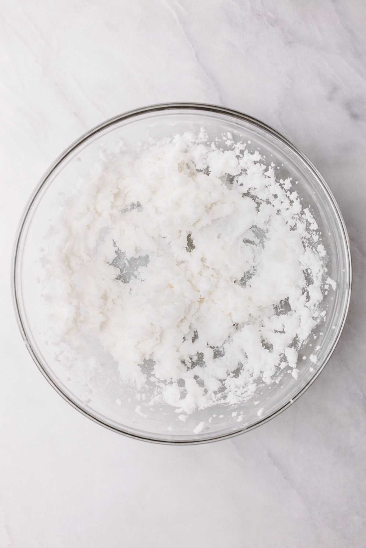 Vegetable shortening and granulated sugar beaten together in a large glass mixing bowl on a light grey textured background.