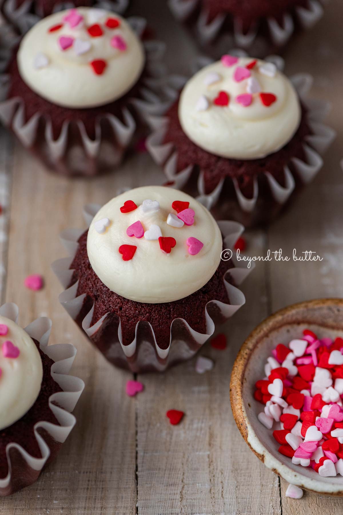 Homemade red velvet cupcakes with cream cheese frosting topped with heart sprinkles on a light wood background | All images © Luyiz®