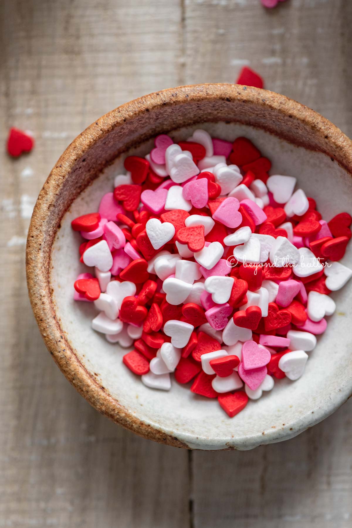 Small bowl of Valentine's Day heart sprinkles Homemade red velvet cupcakes with one opened and half eaten with a small bowl of Valentine's Day sprinkles on light wood background | All images © Luyiz®