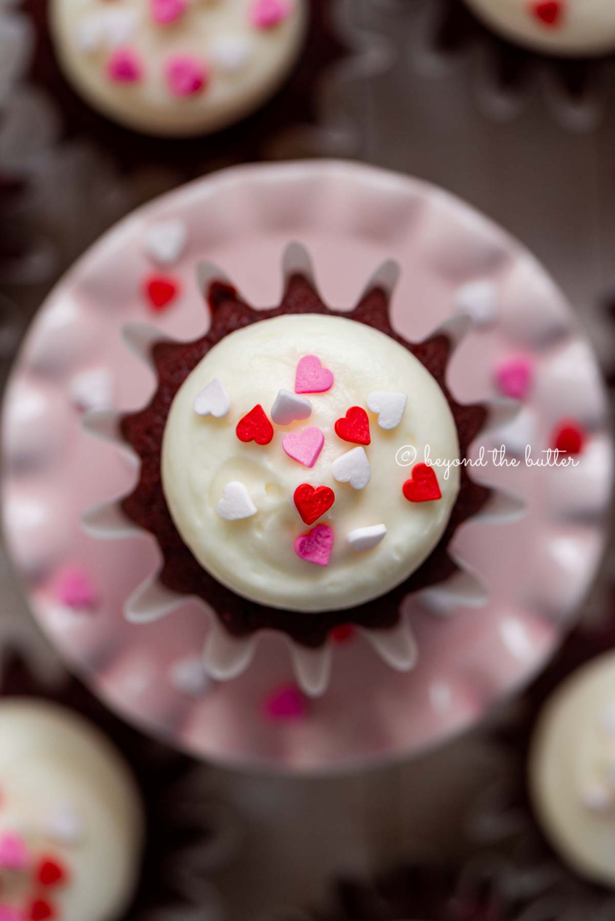 Homemade red velvet cupcakes with cream cheese frosting topped with heart sprinkles on a a small pink cupcake stand | All images © Luyiz®