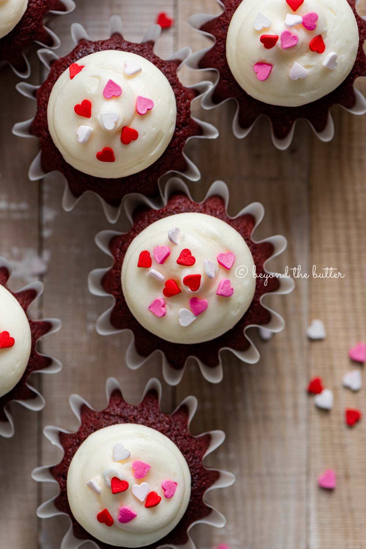 Homemade red velvet cupcakes with cream cheese frosting topped with heart sprinkles on a light wood background | All images © Luyiz®