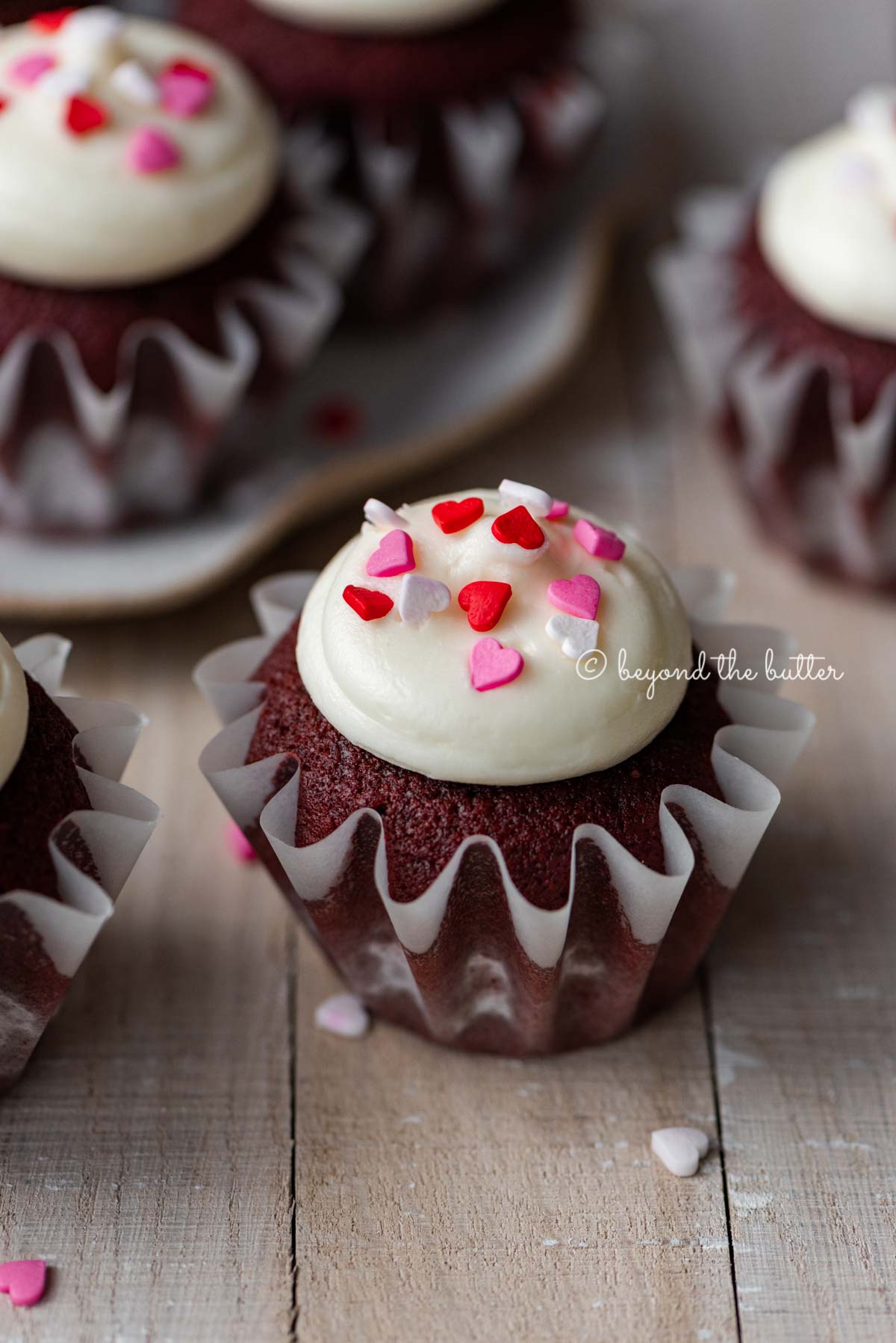 Homemade red velvet cupcakes with cream cheese frosting topped with heart sprinkles on a light wood background | All images © Luyiz®