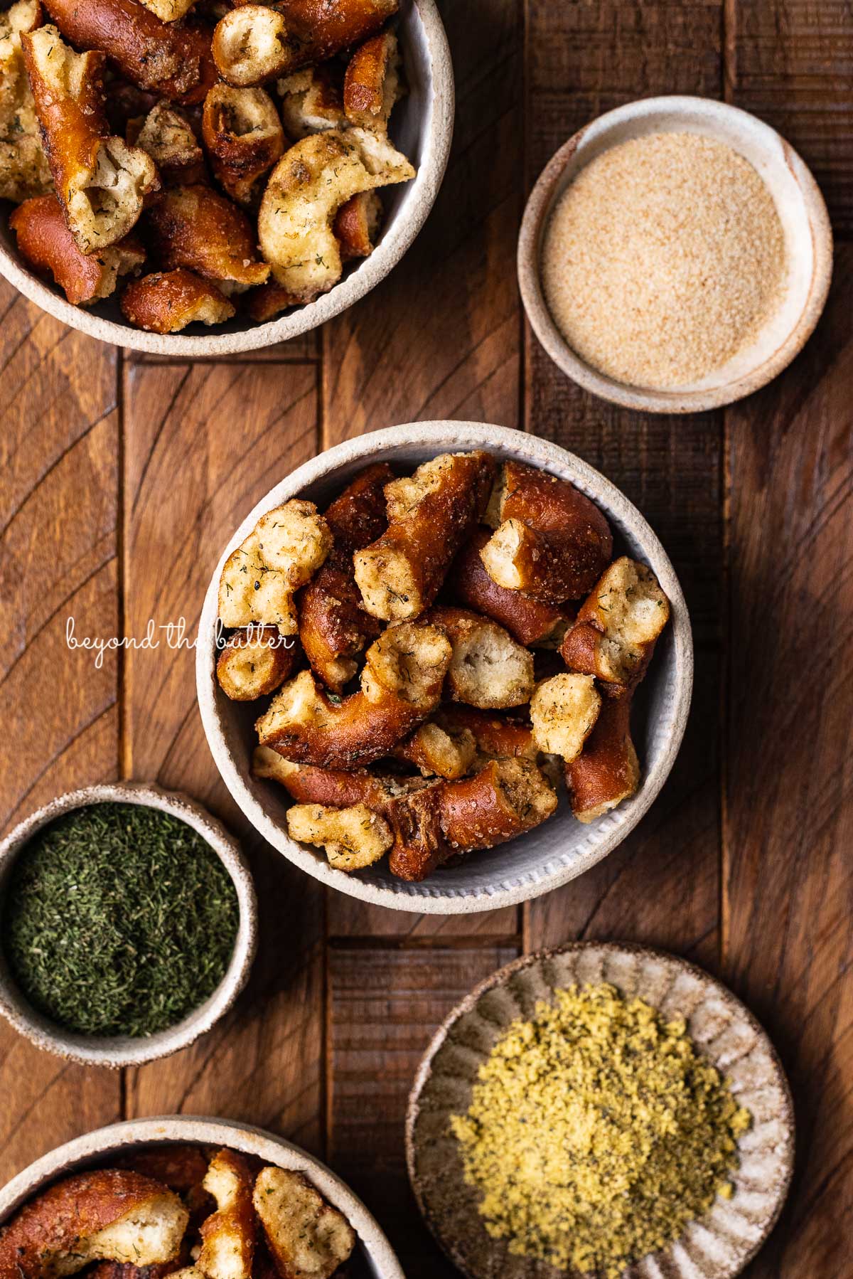 Small ceramic snacking bowls filled with seasoned pretzels with dill weed and garlic powder in side bowl on dark wood background from Luyiz | © Luyiz
