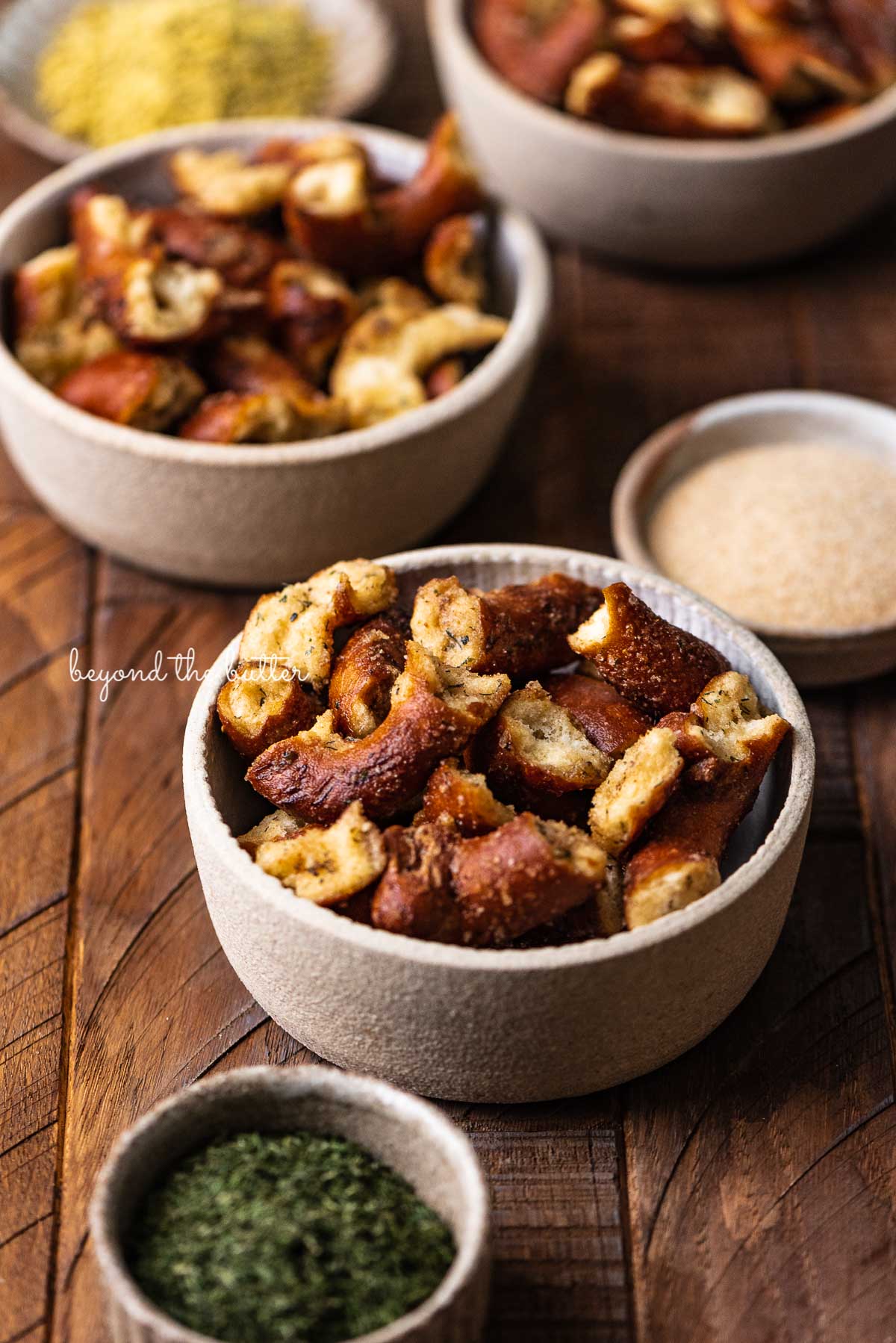 Small snacking bowls filled with seasoned pretzels with dill weed and garlic powder in side bowl on dark wood background from Luyiz | © Luyiz