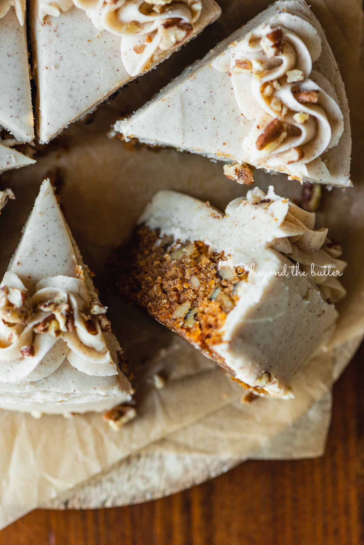 Overhead closeup image of single layer carrot cake frosted on parchment paper and placed on a wood dining room table | All Images © Luyiz®