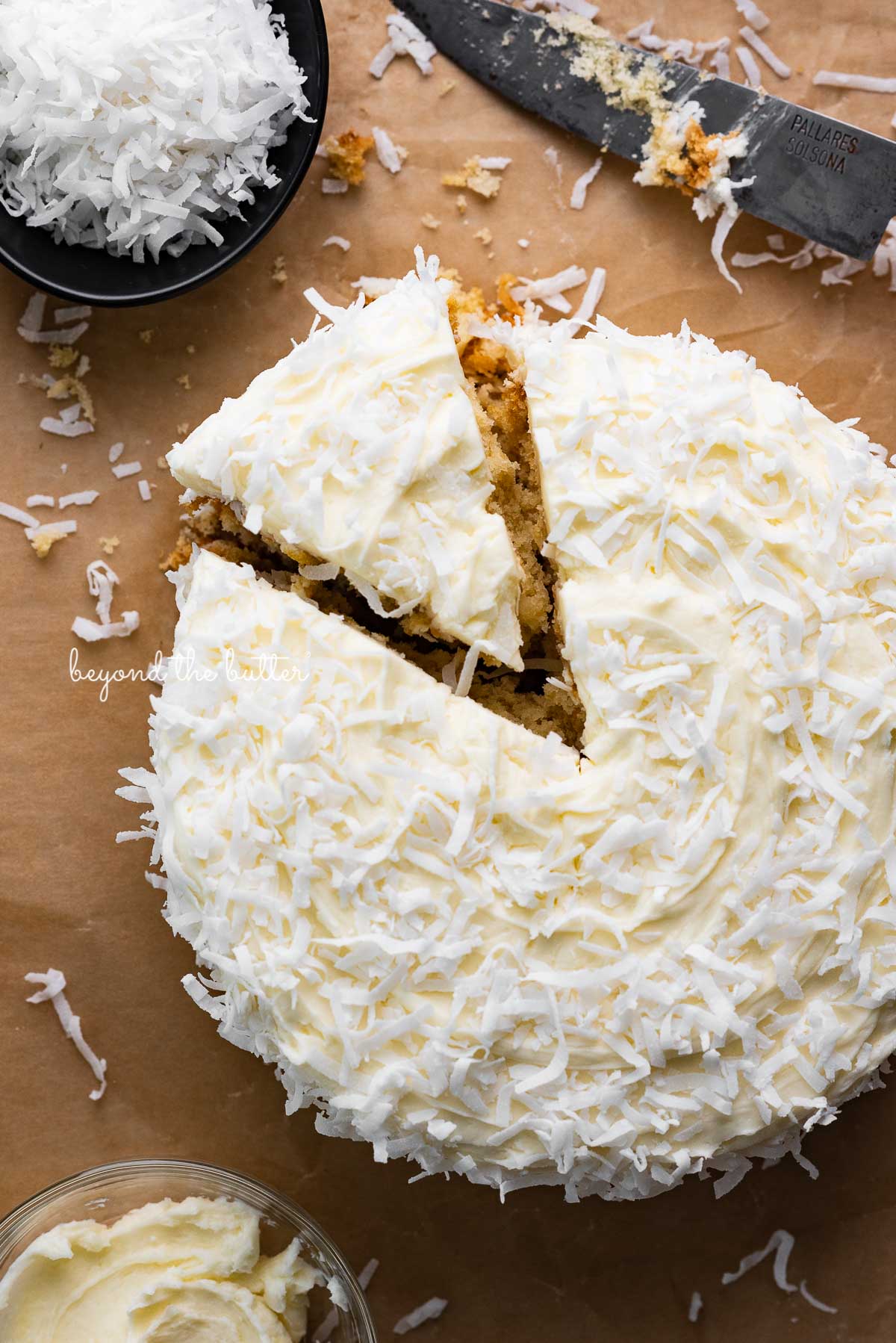 Single layer coconut cake frosted with coconut buttercream with slice cut out on natural parchment paper background | © Luyiz®
