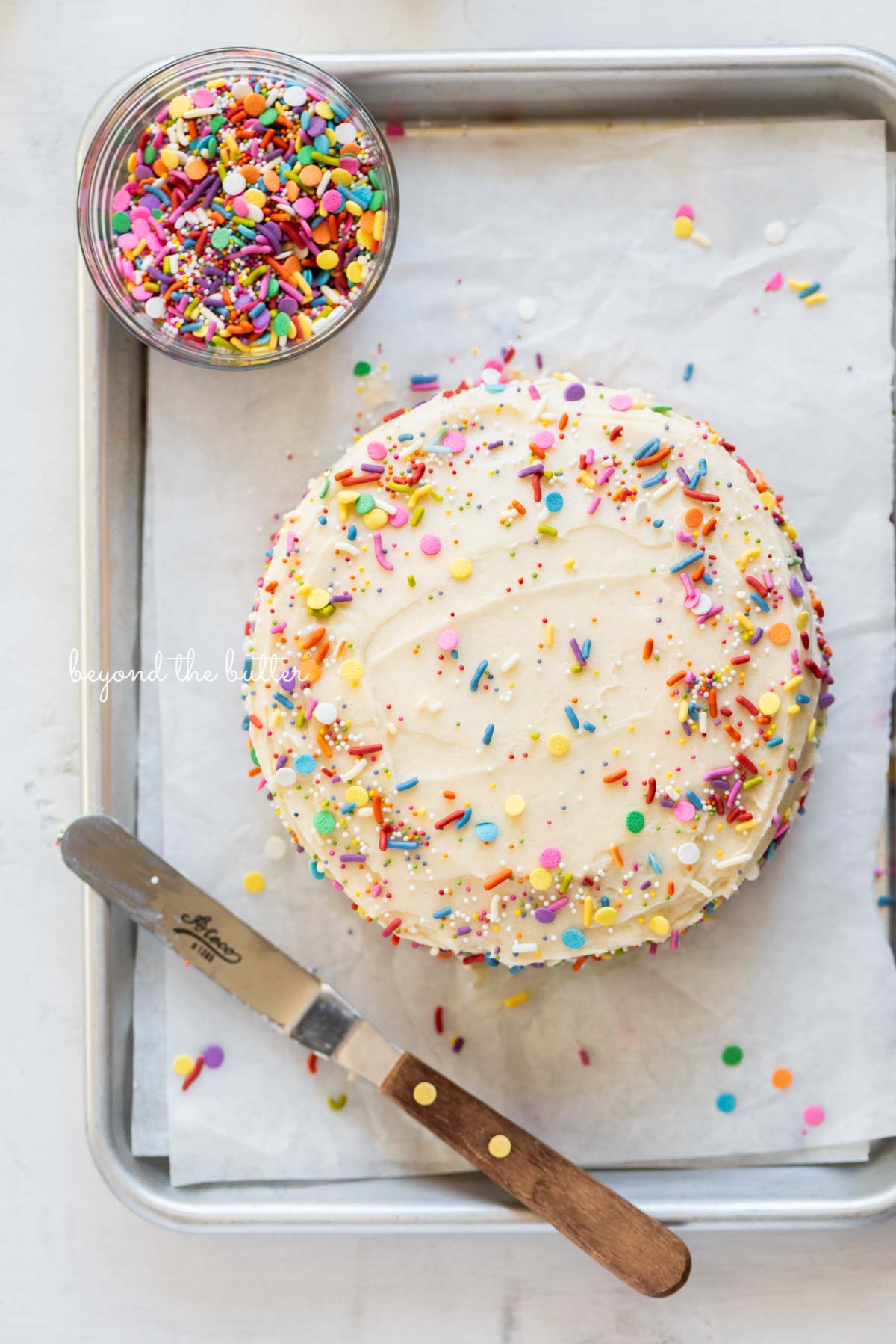 Single layer funfetti cake just frosted and sprinkled on a small parchment paper lined baking sheet from Luyiz | All images © Luyiz®