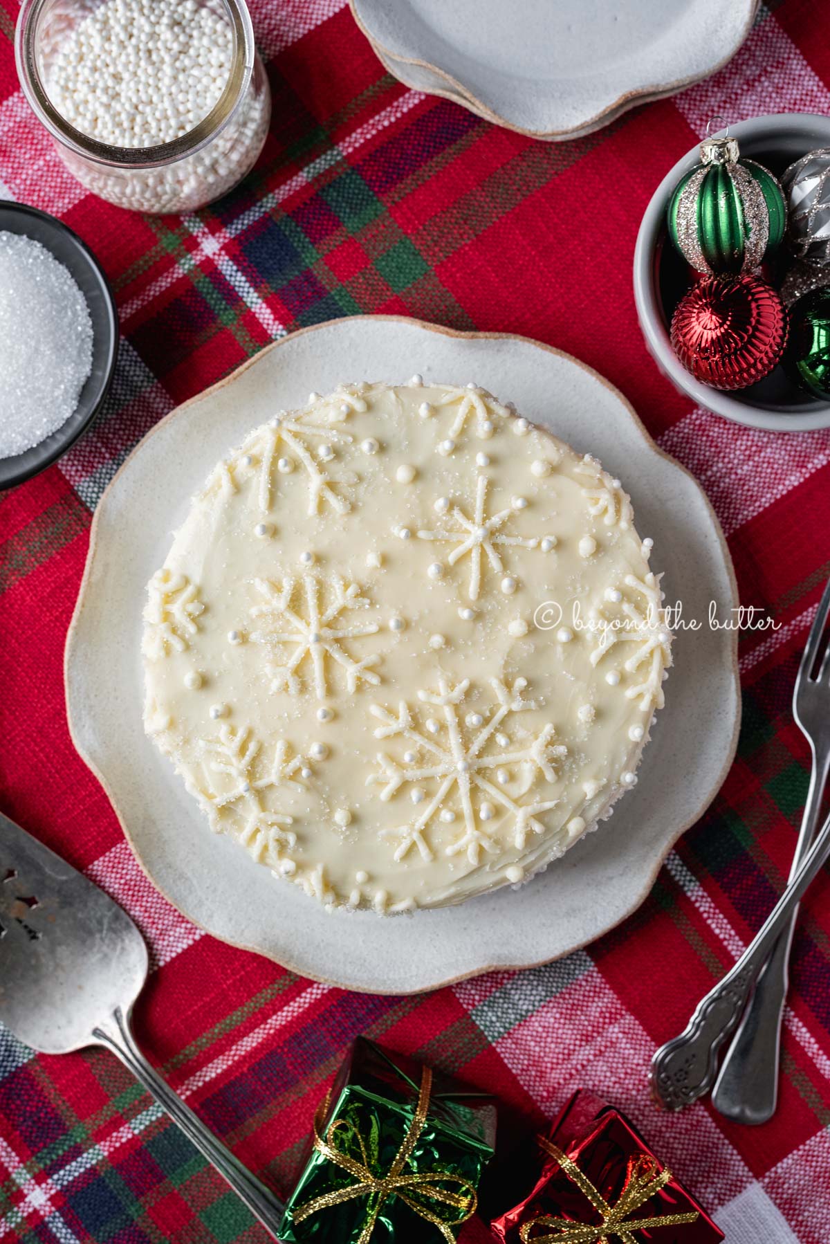 Red velvet cake with cream cheese frosting on a scalloped edge dessert plate with red plaid background | All Images © Luyiz®