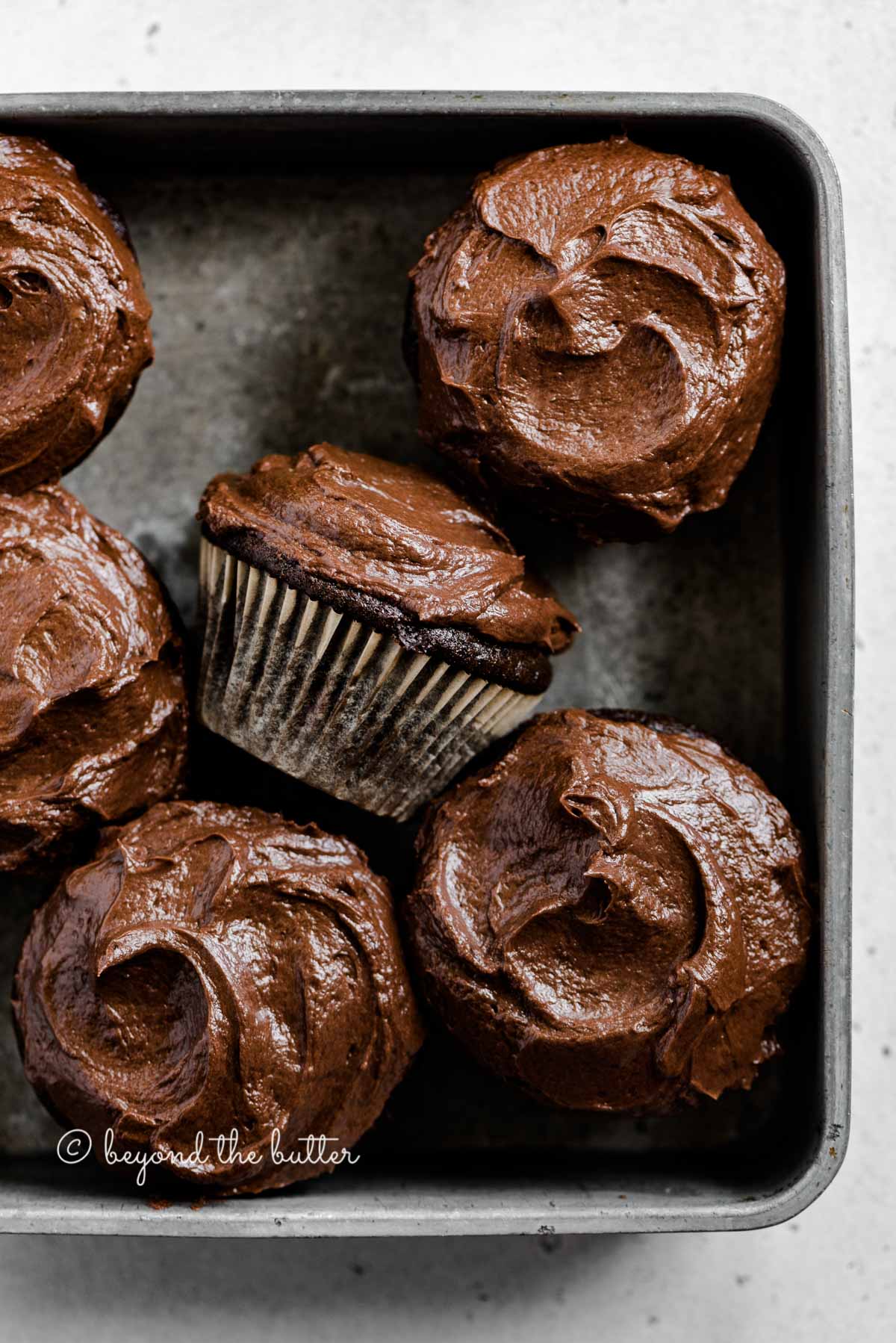 Overhead image of small batch chocolate cupcakes in vintage metal baking tin with one on its side | All Images © Luyiz™