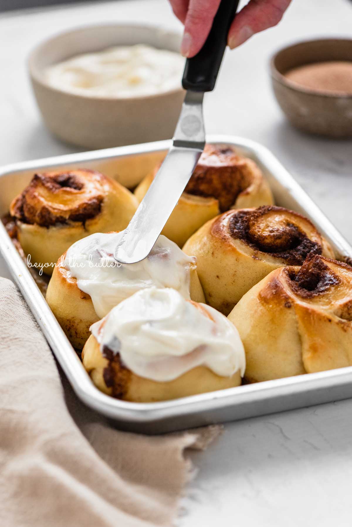Image of small batch cinnamon rolls being frosted with cream cheese frosting from Luyiz | © Luyiz®