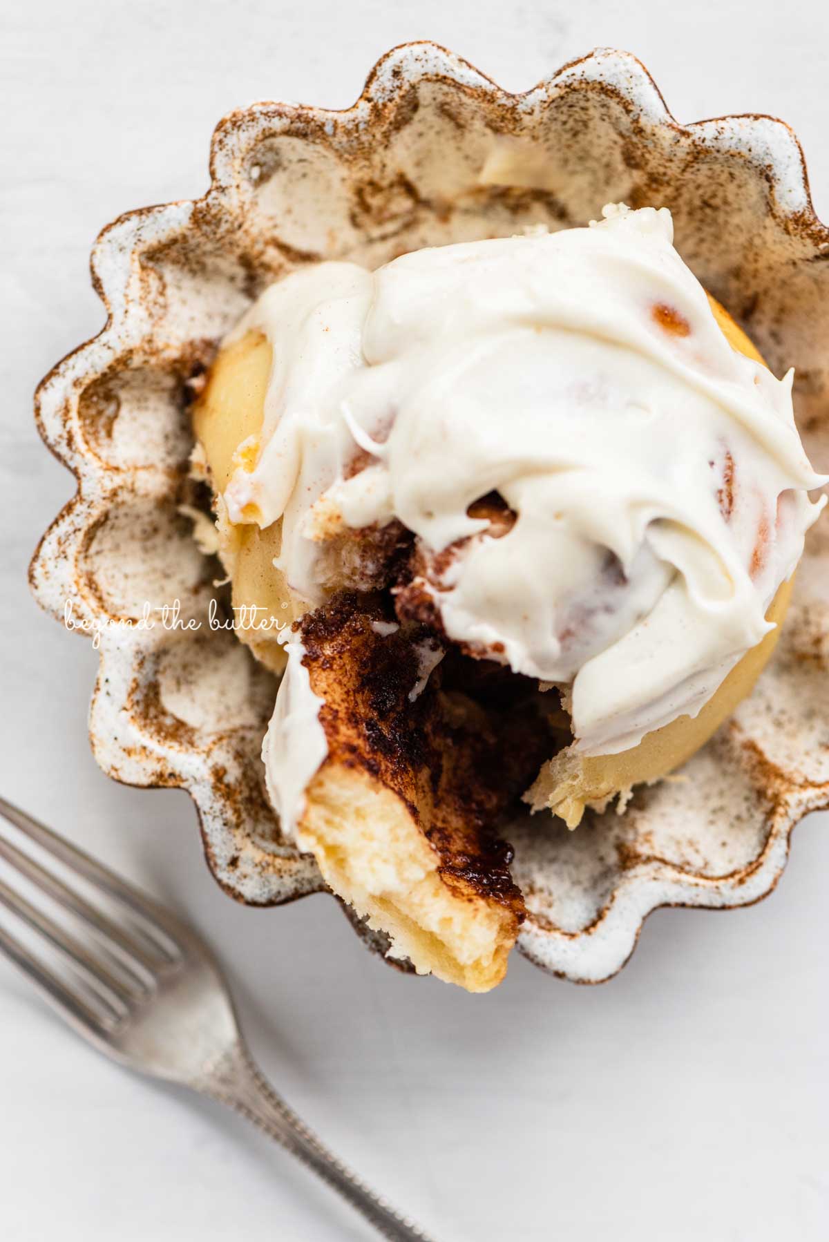 Cream Cheese frosting covered cinnamon roll on small ceramic dessert plate | © Luyiz®
