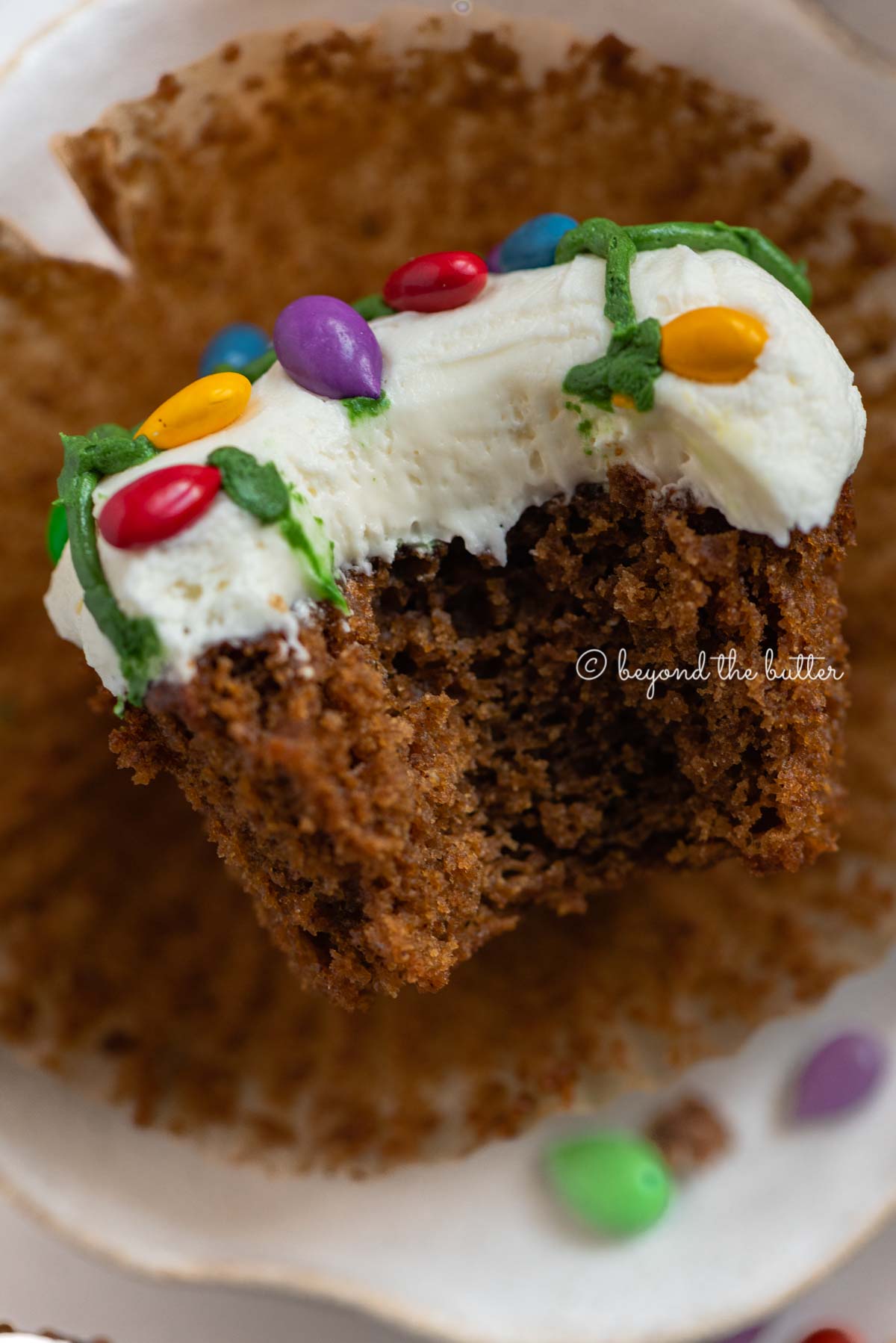 Liner removed with bite taken out of it gingerbread cupcake on a small dessert plate on a white, chocolate covered sunflower seed background | All Images © Luyiz®