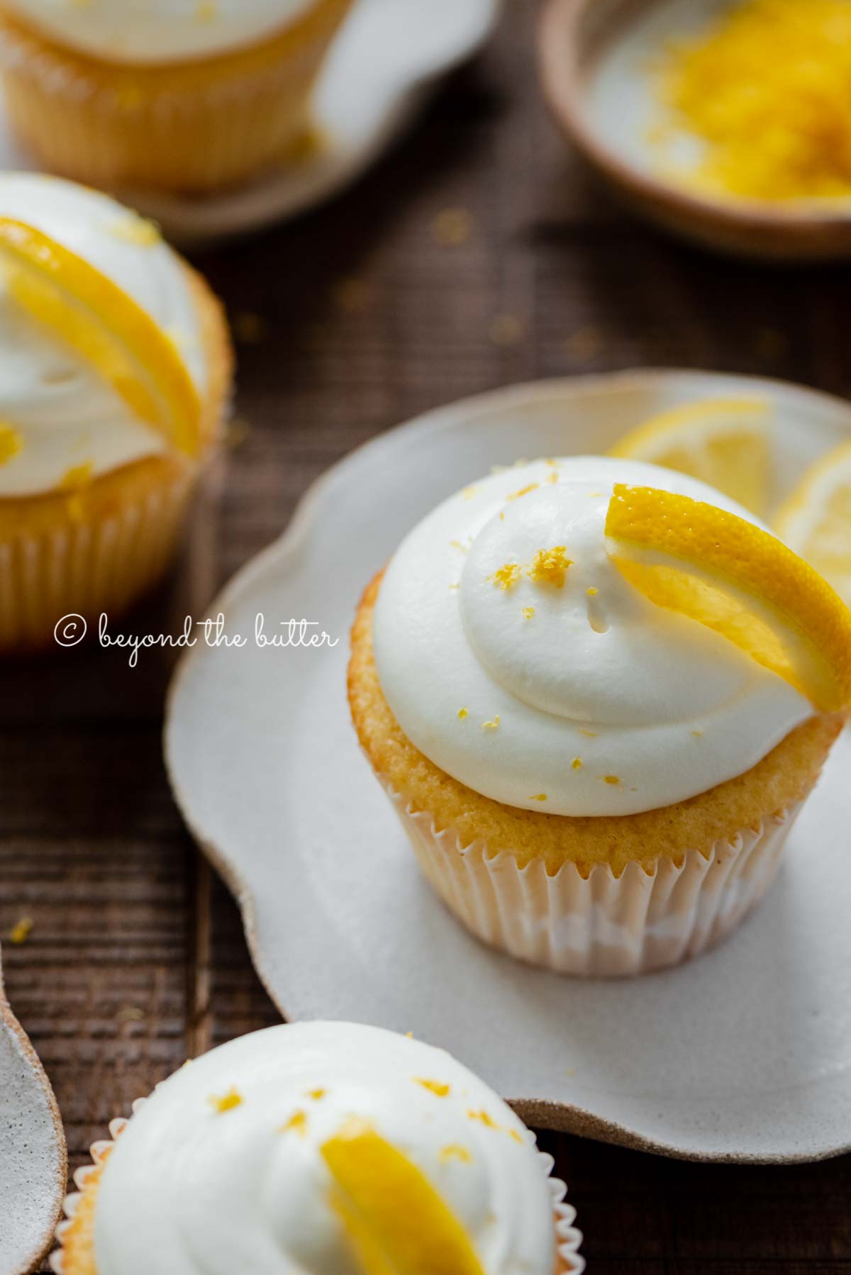 Lemon cupcakes with lemon cream cheese frosting garnished with lemons on small wavy dessert plates | All Images © Luyiz®