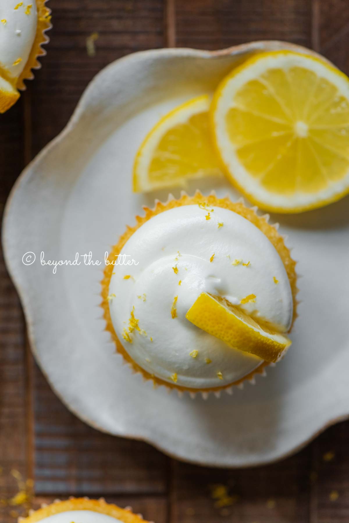 Lemon cupcake with lemon cream cheese frosting garnished with lemons on a small wavy dessert plate | All Images © Luyiz®