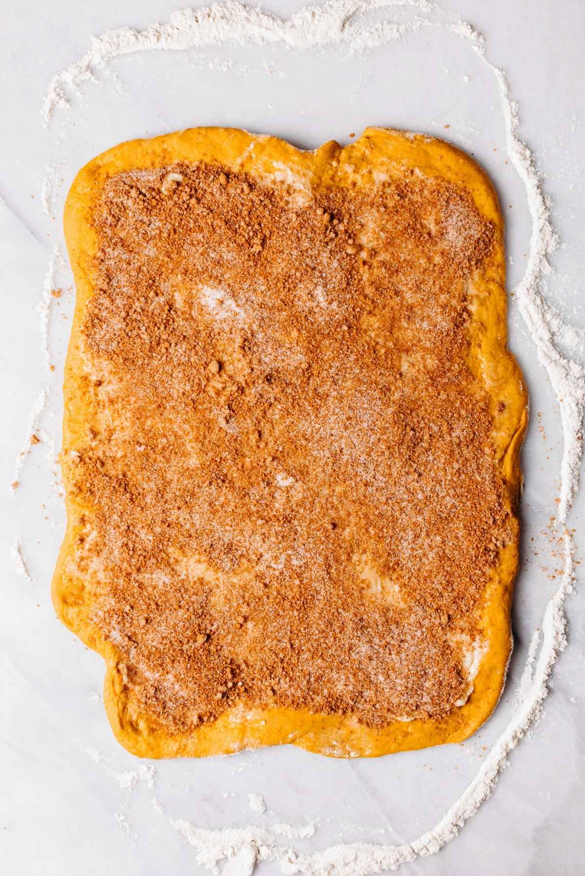 Cinnamon sugar filling and softened butter spread over the top of the rolled out pumpkin cinnamon roll dough.