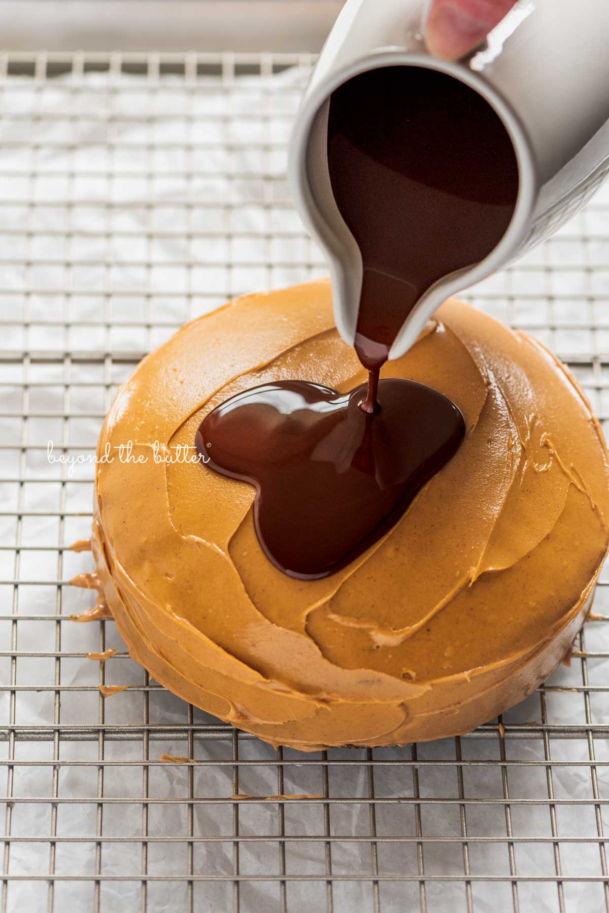 Pouring the melted chocolate over top of the peanut butter layered tandy kake on a wire cooling rack baking sheet | © Luyiz®