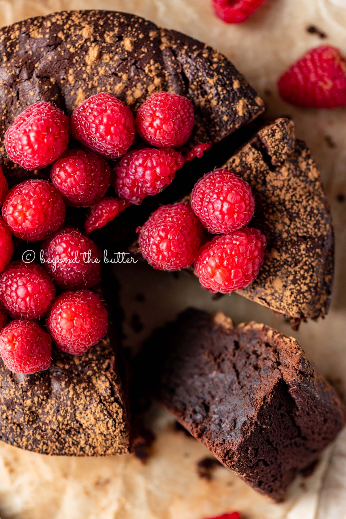Sliced small flourless chocolate cake topped with cocoa powder and fresh raspberries on parchment paper | All images © Luyiz®