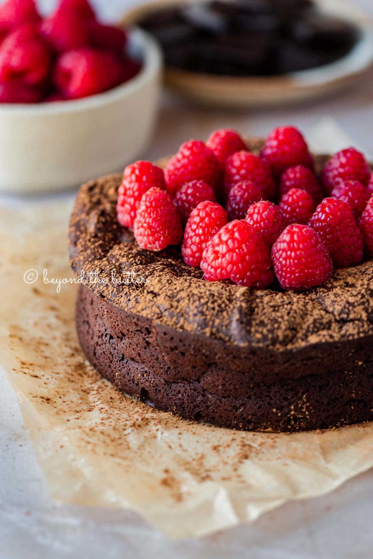 Small flourless chocolate cake topped with cocoa powder and fresh raspberries on parchment paper | All images © Luyiz®