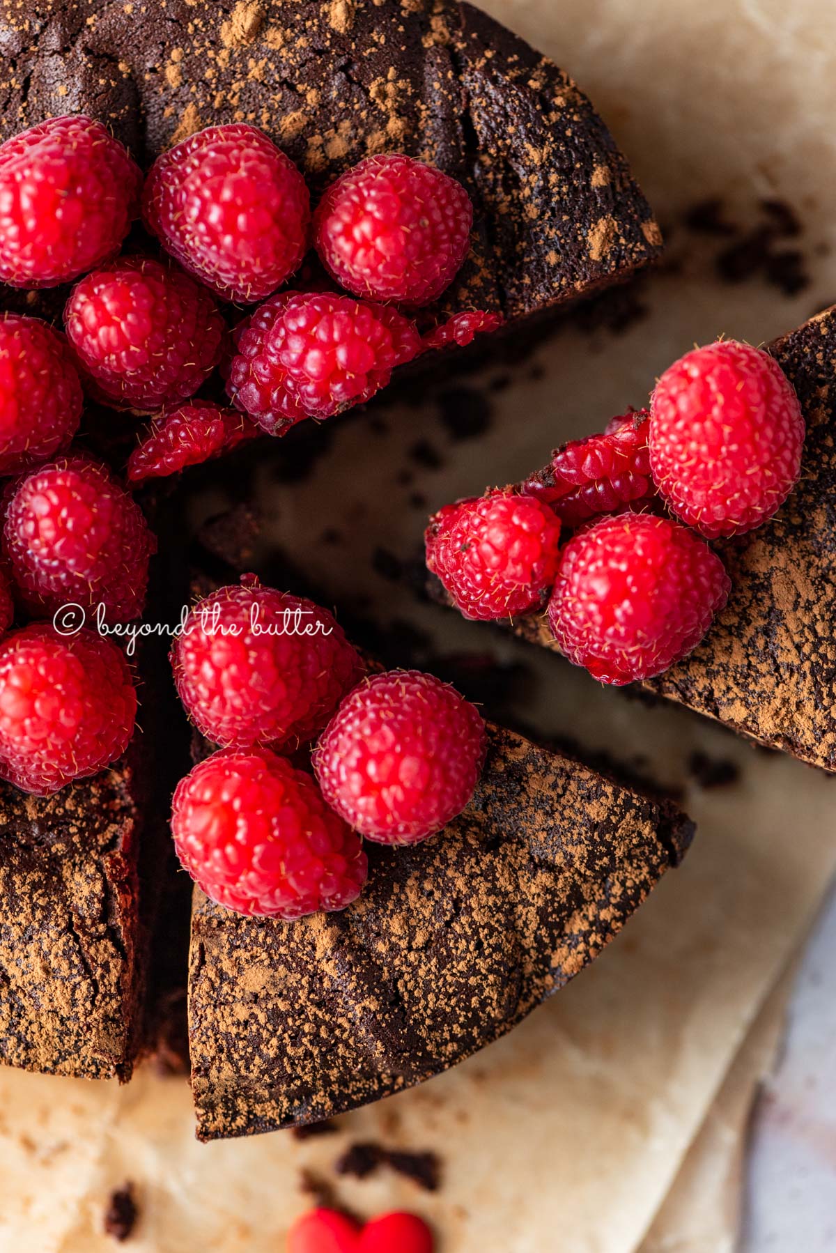 Sliced small flourless chocolate cake topped with cocoa powder and fresh raspberries on parchment paper | All images © Luyiz®