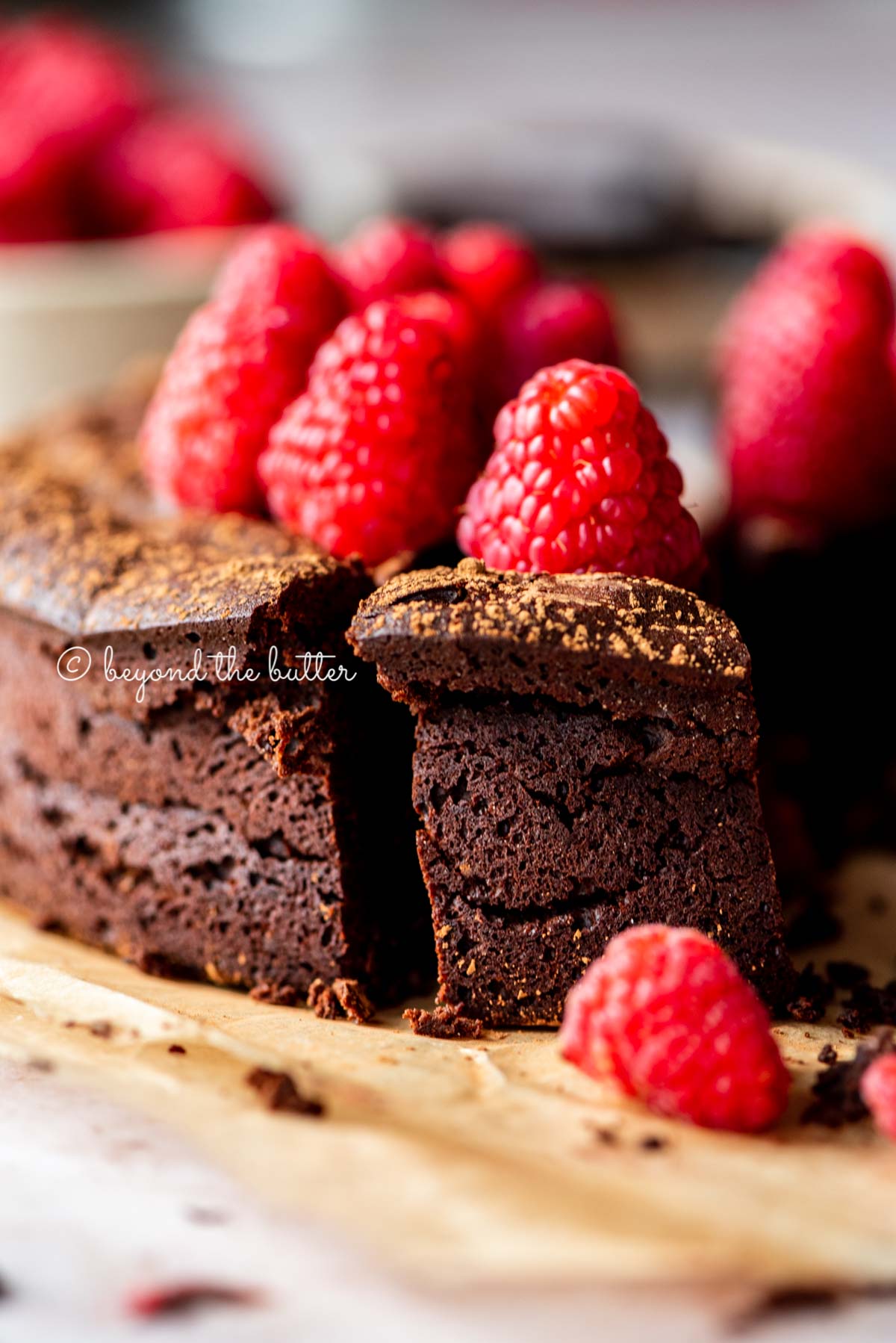 Sliced small flourless chocolate cake topped with cocoa powder and fresh raspberries on parchment paper | All images © Luyiz®