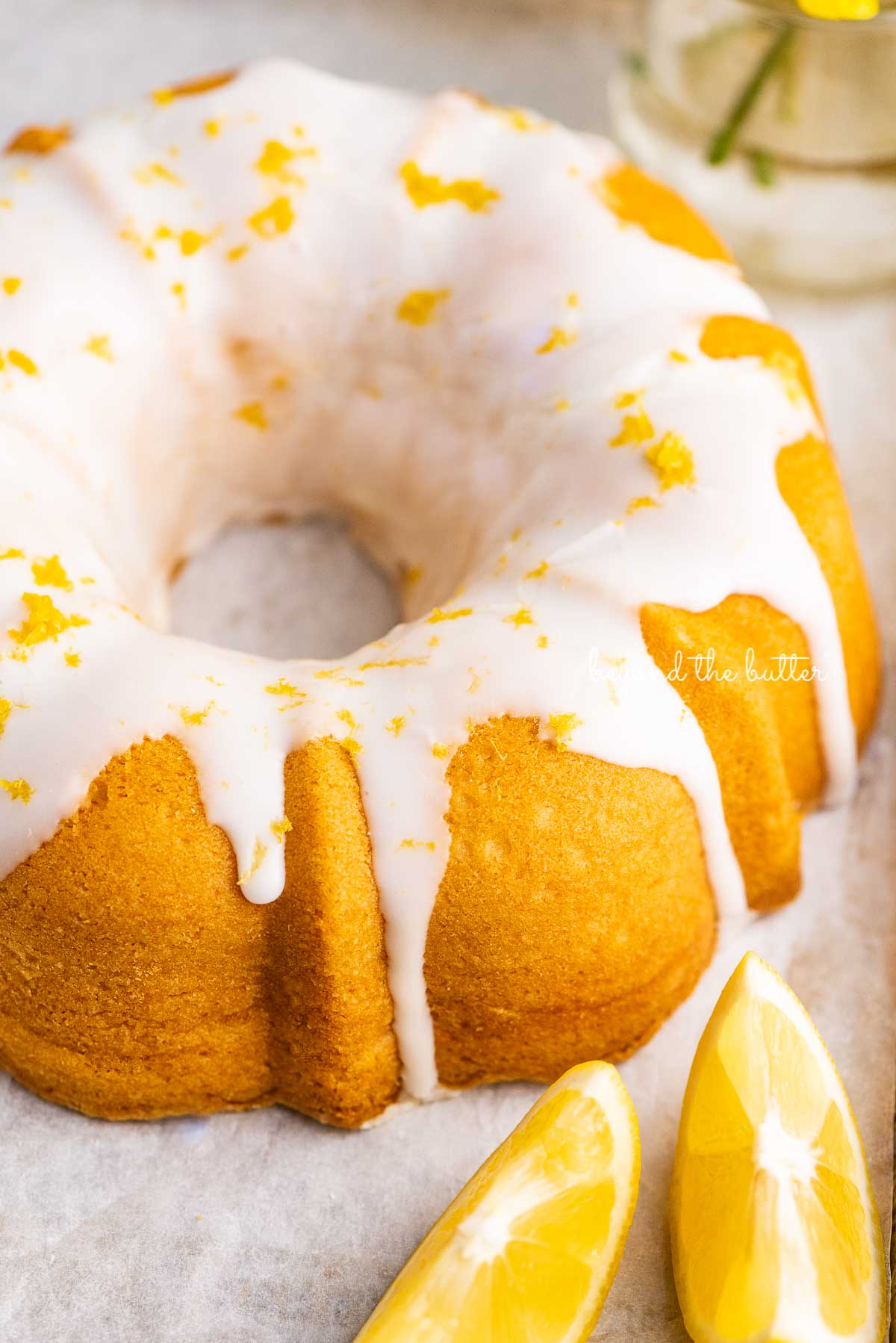 Small lemon cream cheese pound cake topped with a simple lemon glaze on a parchment paper lined baking sheet with sliced lemons | © Luyiz®