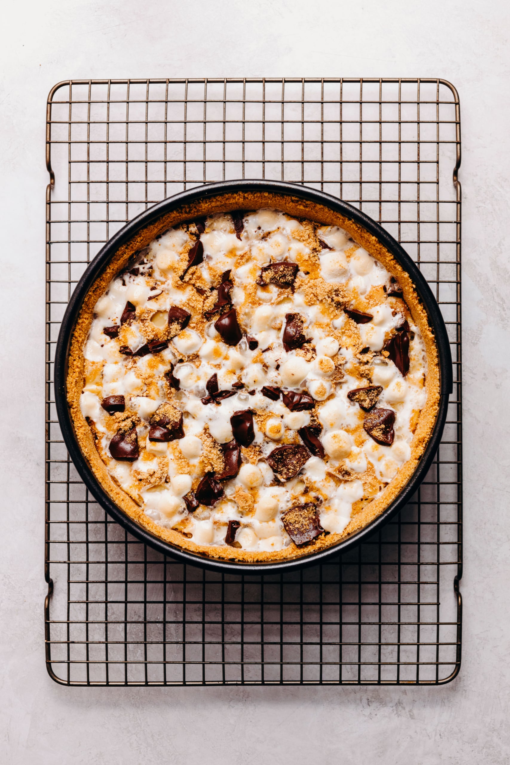Baked s'mores cheesecake cooling on a wire cooling rack on a textured white background.
