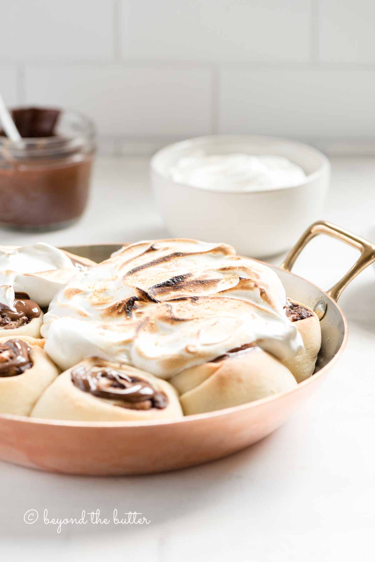 Pan of s'mores rolls on a kitchen counter with bowl of marshmallow topping and melted chocolate | All Images © Luyiz™