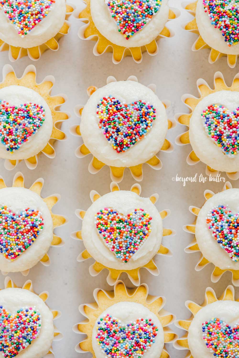 Overhead image of sprinkled heart cupcakes on white/grya background | All Images © Luyiz™