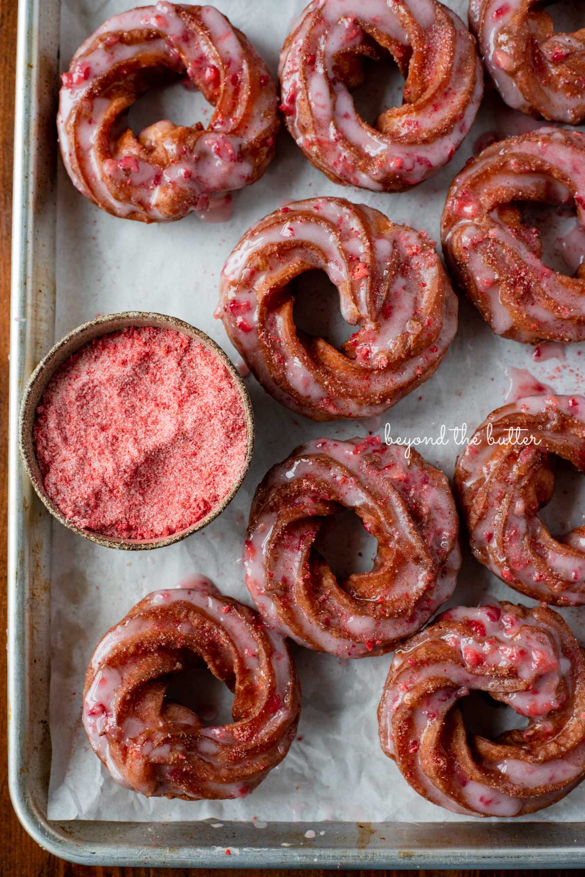 Strawberry glazed french crullers sprinkled with strawberry sugar on a parchment paper lined baking sheet | © Luyiz®