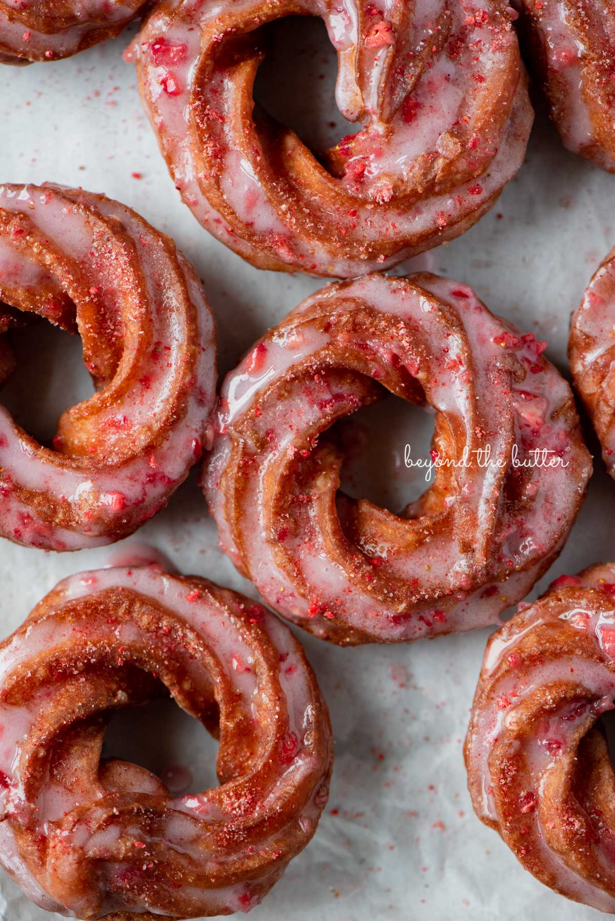 Strawberry glazed french crullers sprinkled with strawberry sugar on a parchment paper lined baking sheet | © Luyiz®
