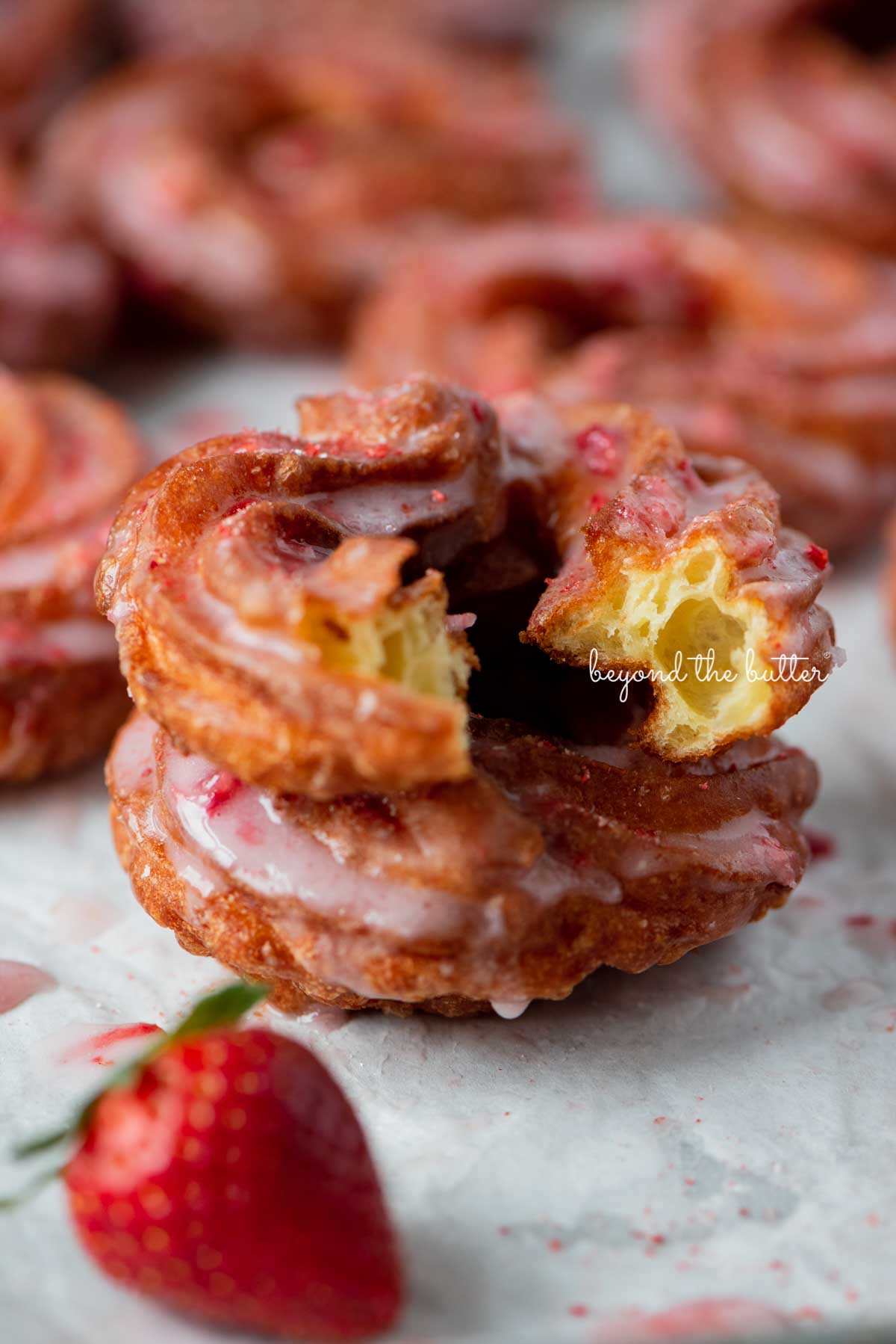 Light and airy stacked strawberry glazed french crullers with cite taken out of the top cruller | © Luyiz®