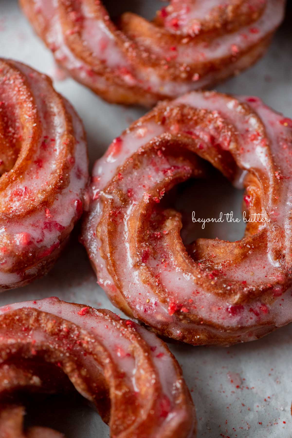 Strawberry glazed french crullers sprinkled with strawberry sugar on a parchment paper lined baking sheet | © Luyiz®