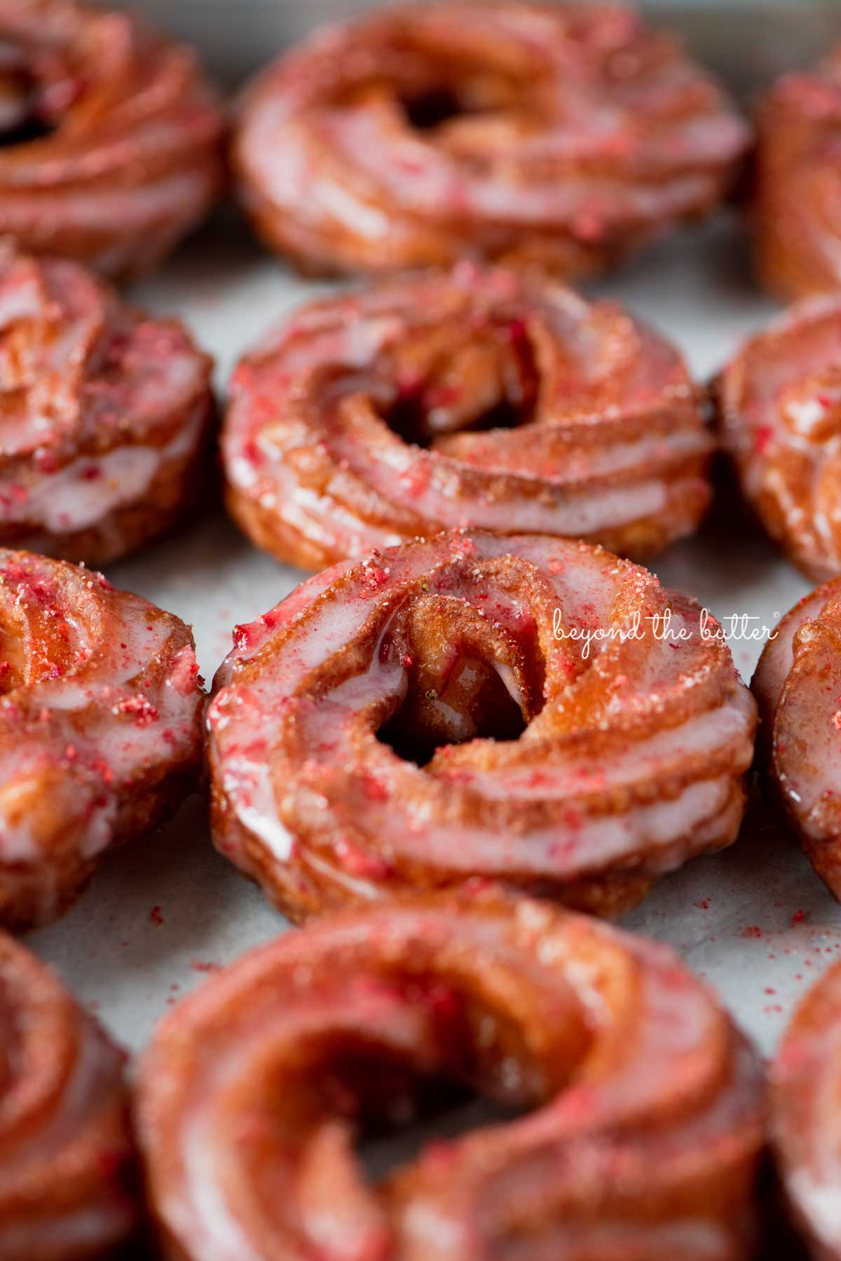 Strawberry glazed french crullers sprinkled with strawberry sugar on a parchment paper lined baking sheet | © Luyiz®
