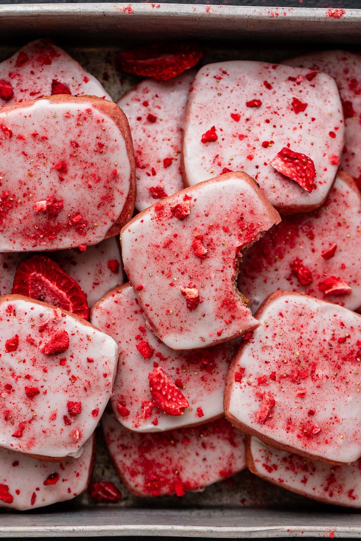 Strawberry shortbread cookies topped with a powdered sugar glaze and freeze dried strawberry bits randomly placed in a vintage baking tin.