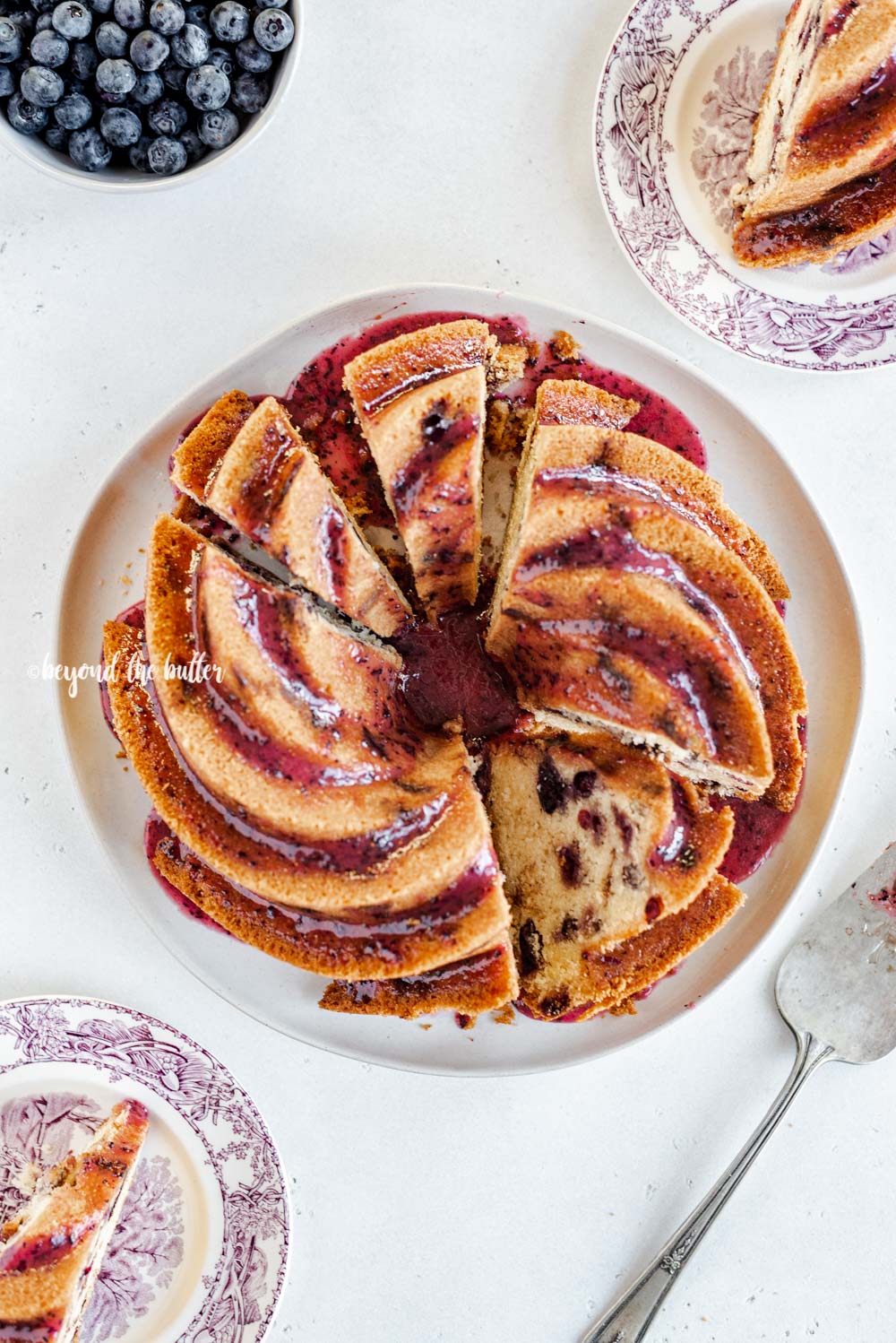 Overhead image of sliced blueberry bundt cake with blueberry glaze drizzled over the top | All Images © Luyiz, LLC