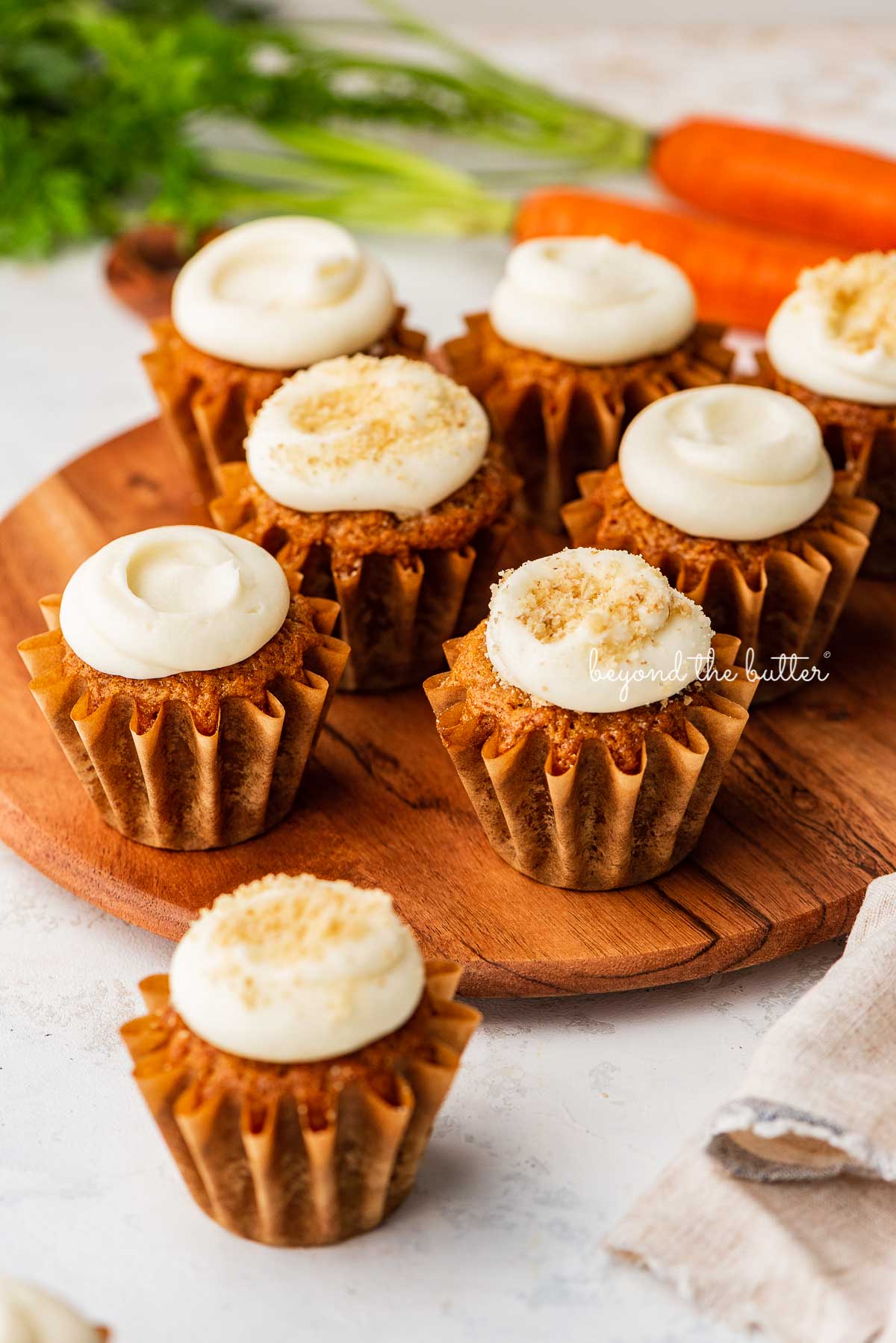 Super moist carrot cake cupcakes with cream cheese frosting placed on a wood cake stand on a white background with some carrots | © Luyiz®