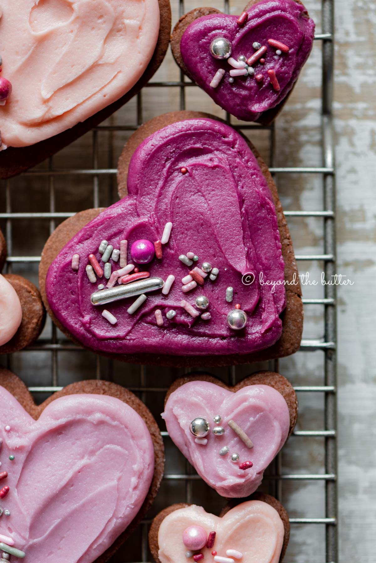 Closeup of decorated chocolate cut out sugar cookies on a wire cooling rack on light wood colored background | All Images © Luyiz®