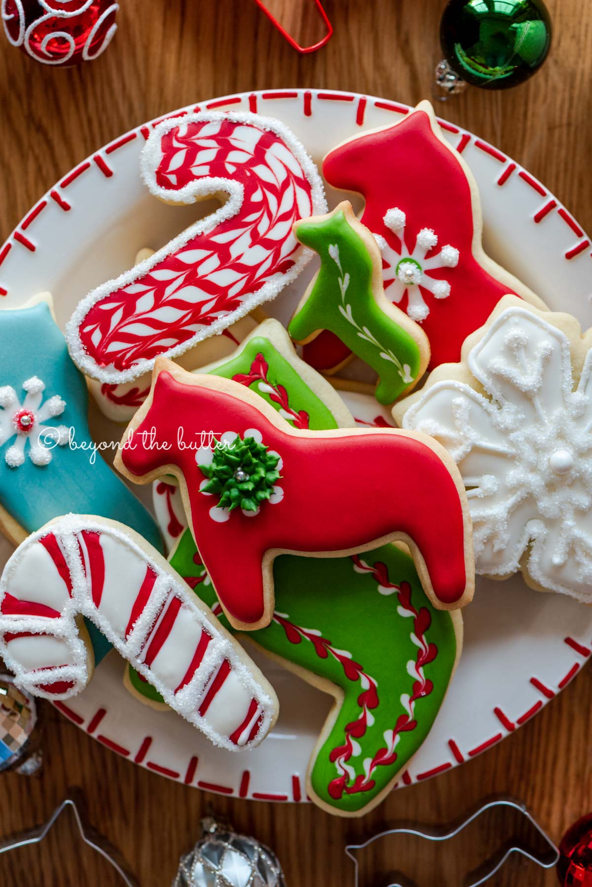 Plate of super soft cut out sugar cookies with royal icing with ornaments and cookie cutters around it | All Images © Luyiz®