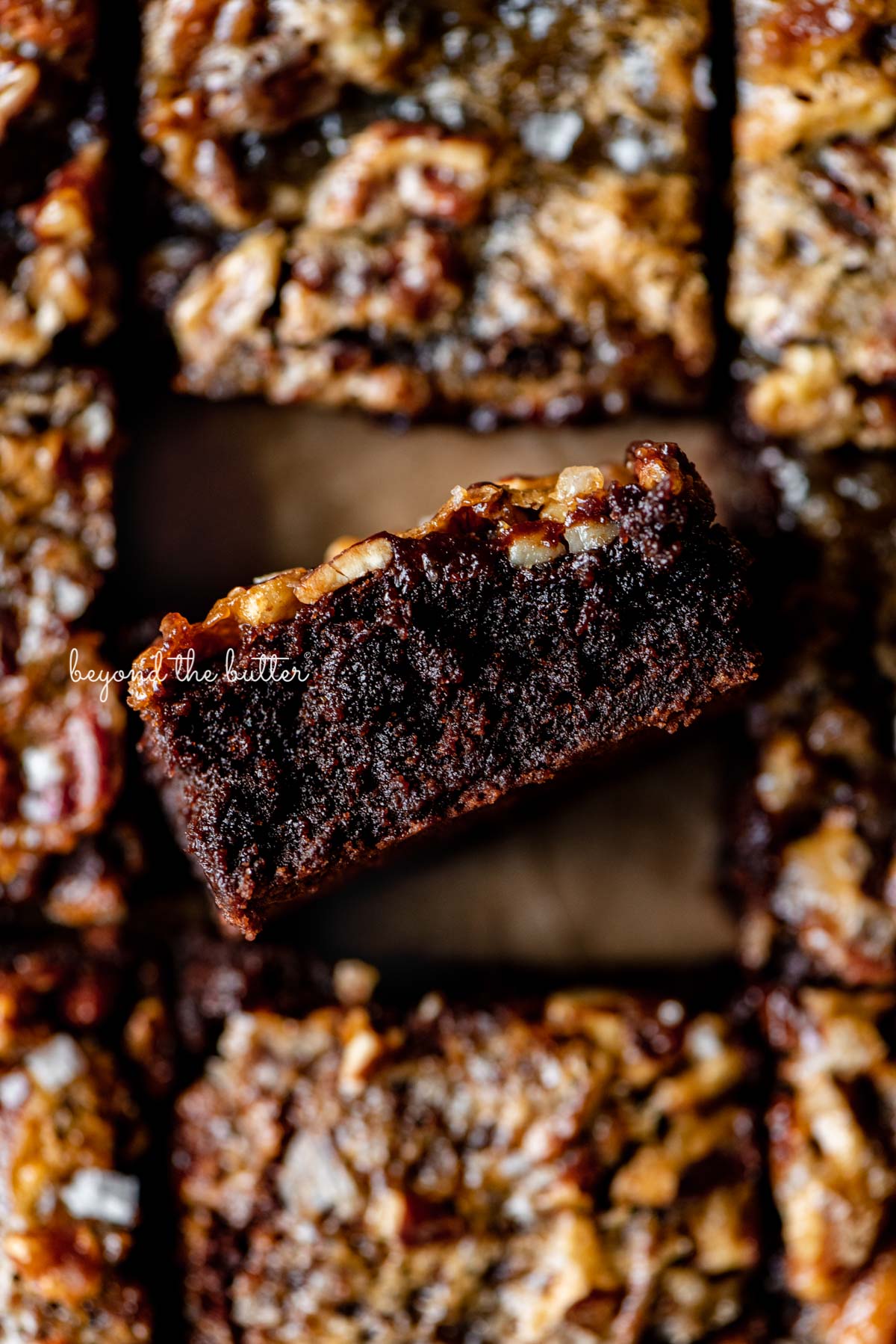 Salted pecan pie brownies placed on brown parchment paper with the center brownie placed on its side | © Luyiz®