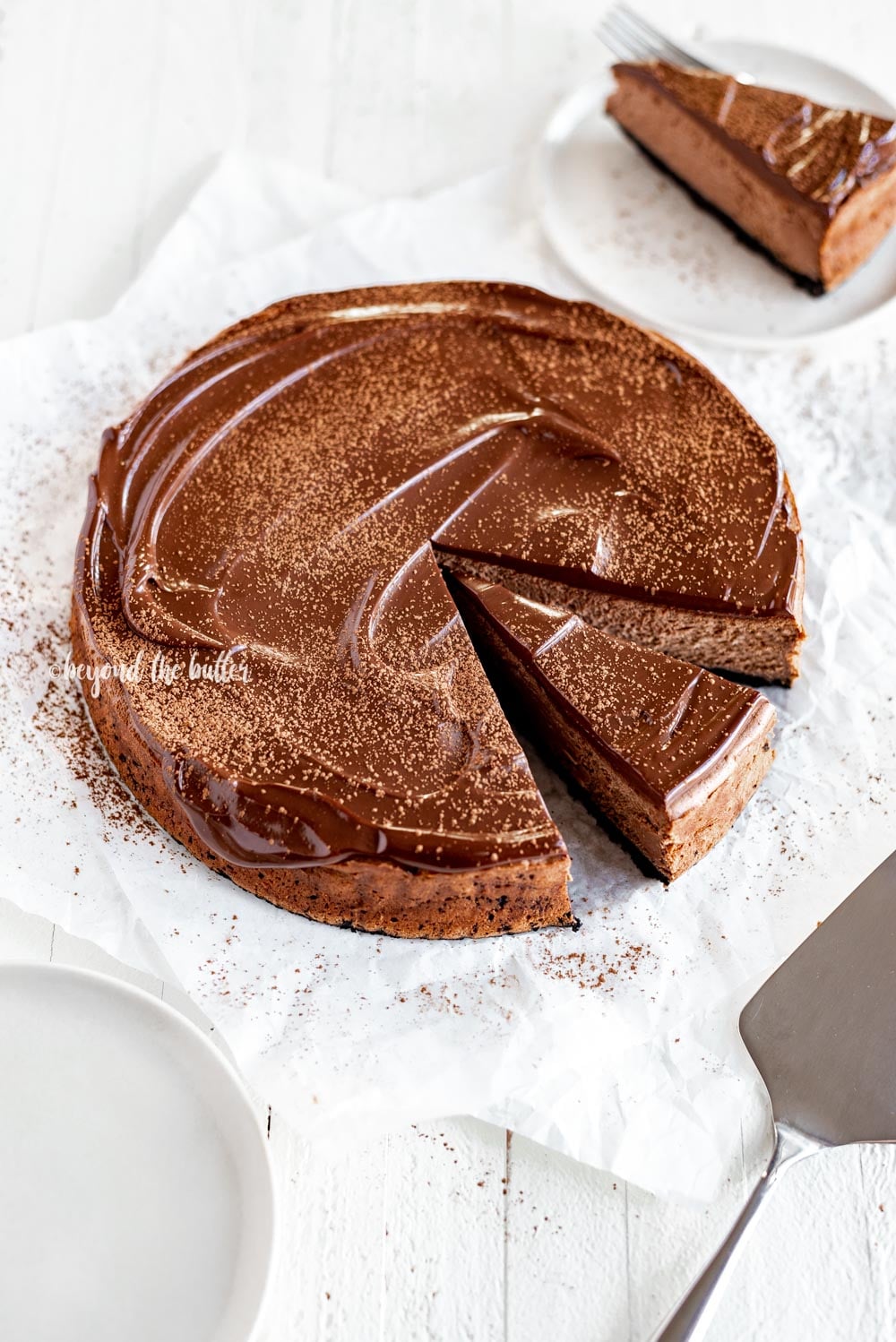 Overhead angled image of Triple Chocolate Mocha Cheesecake dusted with cocoa and a slice removed | All Images © Luyiz, LLC