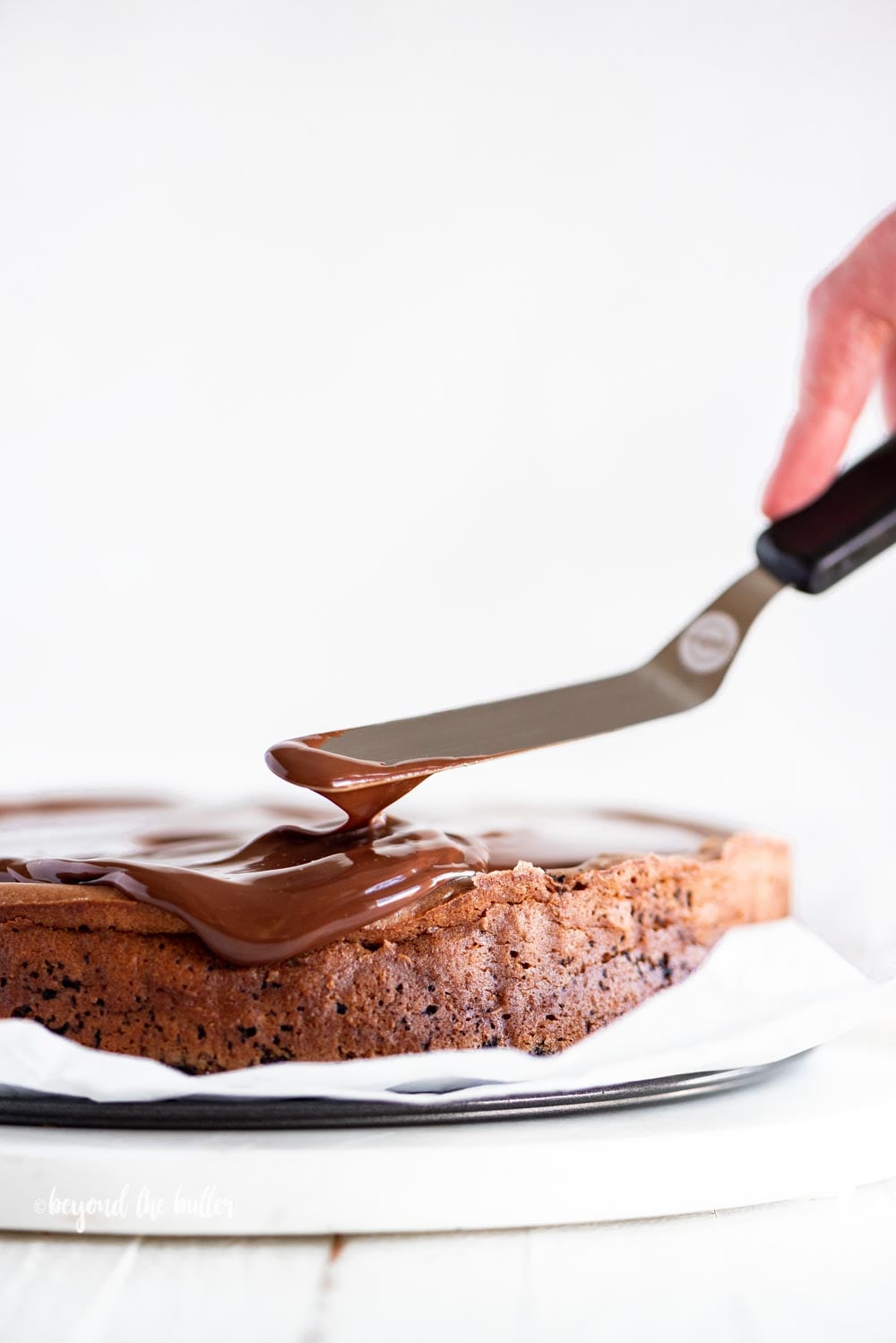 Using an offset spatula to spread out the dark chocolate ganache on top of the Triple Chocolate Mocha Cheesecake | All Images © Luyiz, LLC