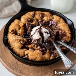 Brown Butter Chocolate Chip Skillet Cookie Recipe 11 Warm chocolate chip skillet cookie with scoop of vanilla ice cream and two spoons resting in skillet on wood trivet.