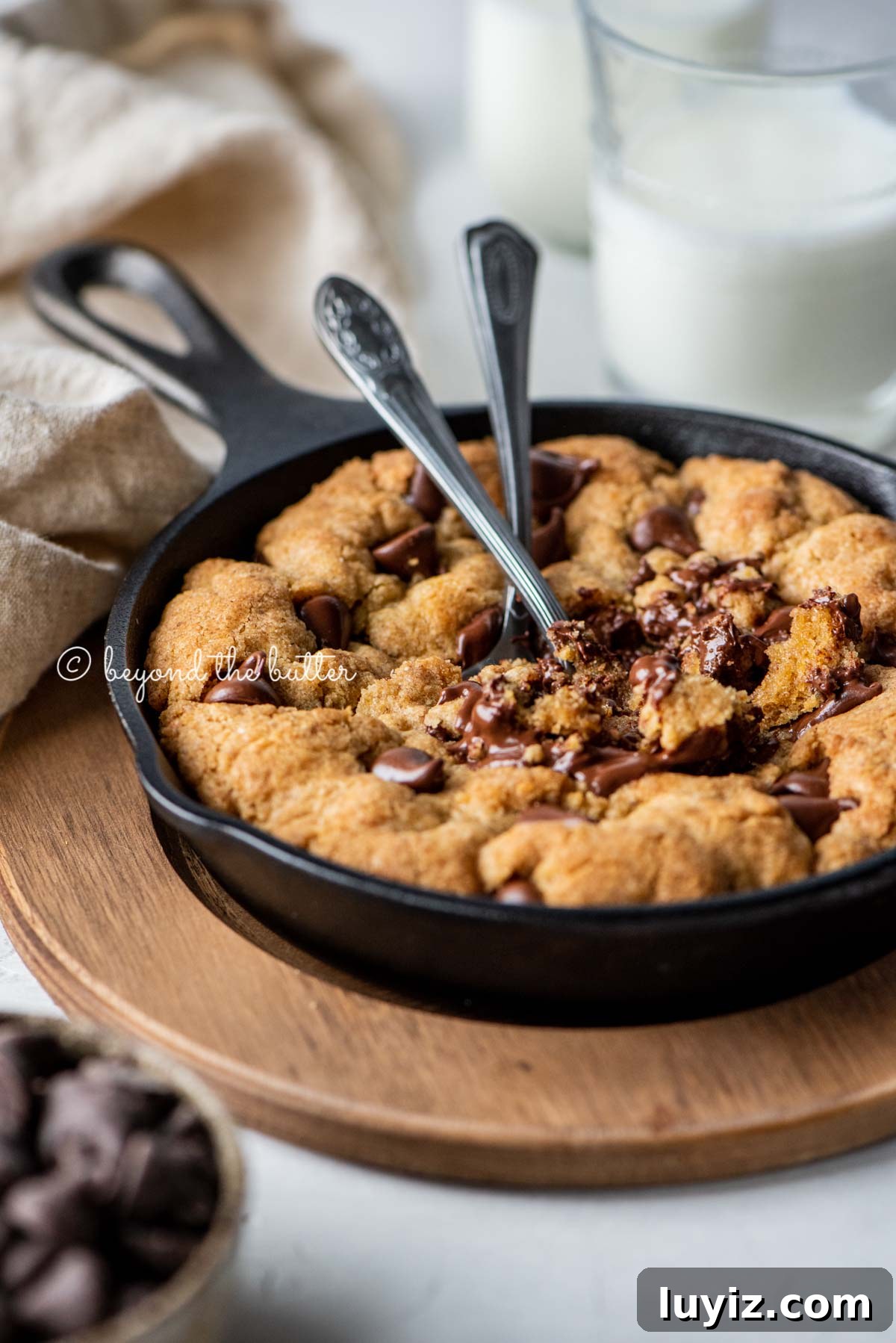 Brown Butter Chocolate Chip Skillet Cookie Recipe 5 Warm brown butter chocolate chip skillet cookie with two spoons resting in skillet on wood trivet