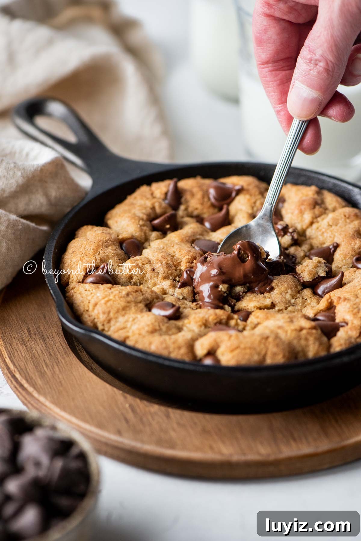 Brown Butter Chocolate Chip Skillet Cookie Recipe 6 Warm brown butter chocolate chip skillet cookie with two spoons resting in skillet on wood trivet