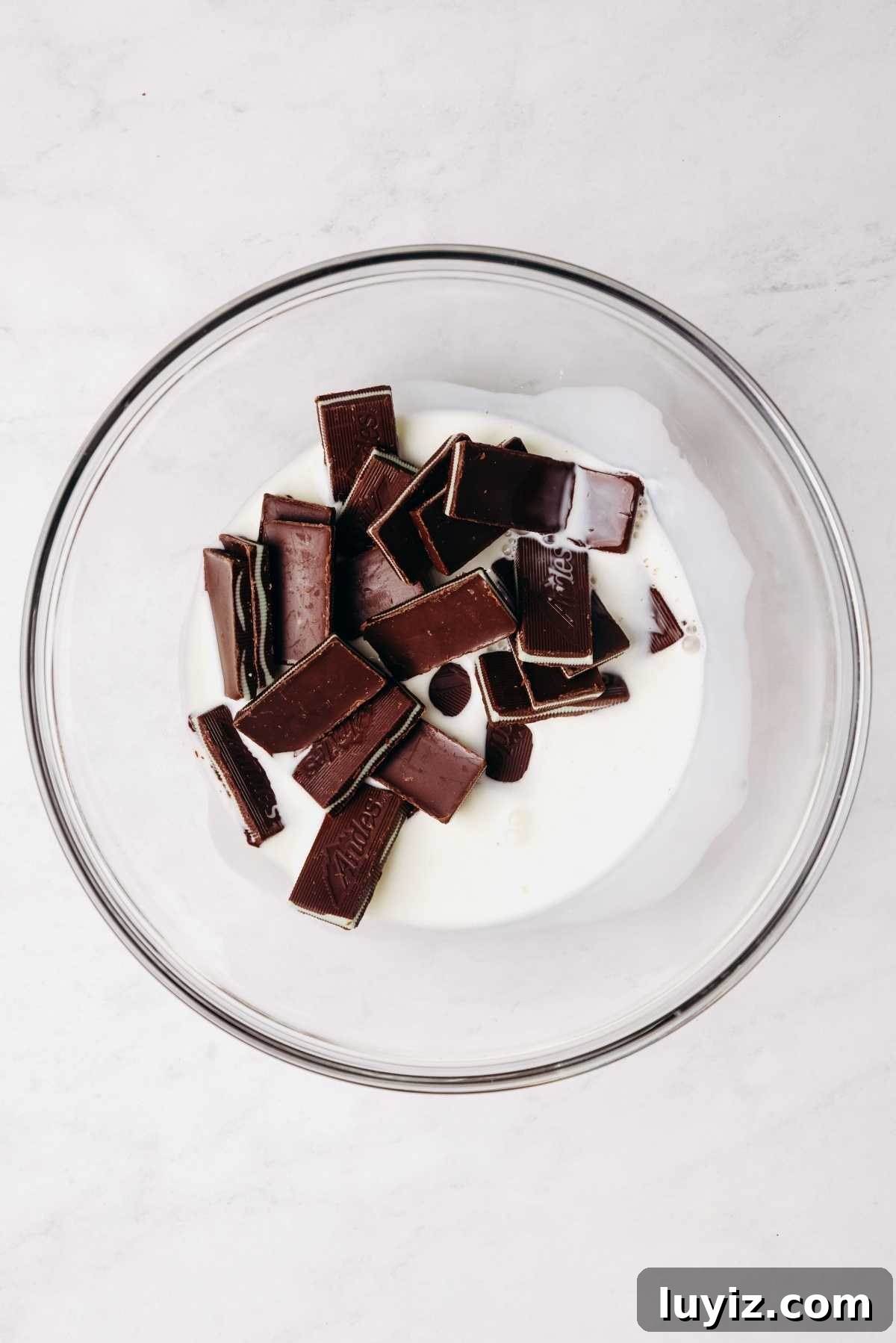 Mint Chocolate Cupcake Recipe: Moist Chocolate Cakes with Minty Frosting 9 Andes mint chocolates and heavy cream in a small glass mixing bowl on a grey marbled background.