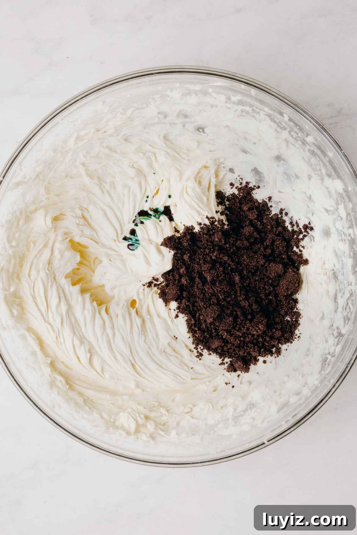 Mint Chocolate Cupcake Recipe: Moist Chocolate Cakes with Minty Frosting 12 Heavy cream, green food coloring, and crushed chocolate cookies added to the top of mint chocolate oreo buttercream frosting in large glass mixing bowl.