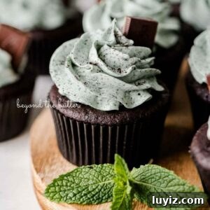 Mint Chocolate Cupcake Recipe: Moist Chocolate Cakes with Minty Frosting 22 Mint chocolate cupcakes topped with mint chocolate chip frosting and an Andes mint on a wood circular tray with mint leaves as decoration.