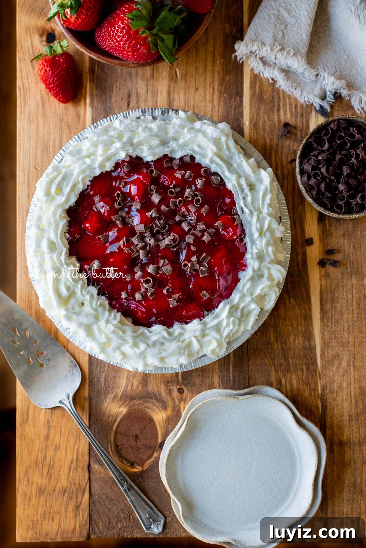 No-Bake Chocolate Strawberry Pie Recipe for Summer Parties 3 Decorated no bake strawberry chocolate pie with small bowl of chocolate curls and strawberries, dessert plates, and pie server on wood table | All images © Beyond the Butter®