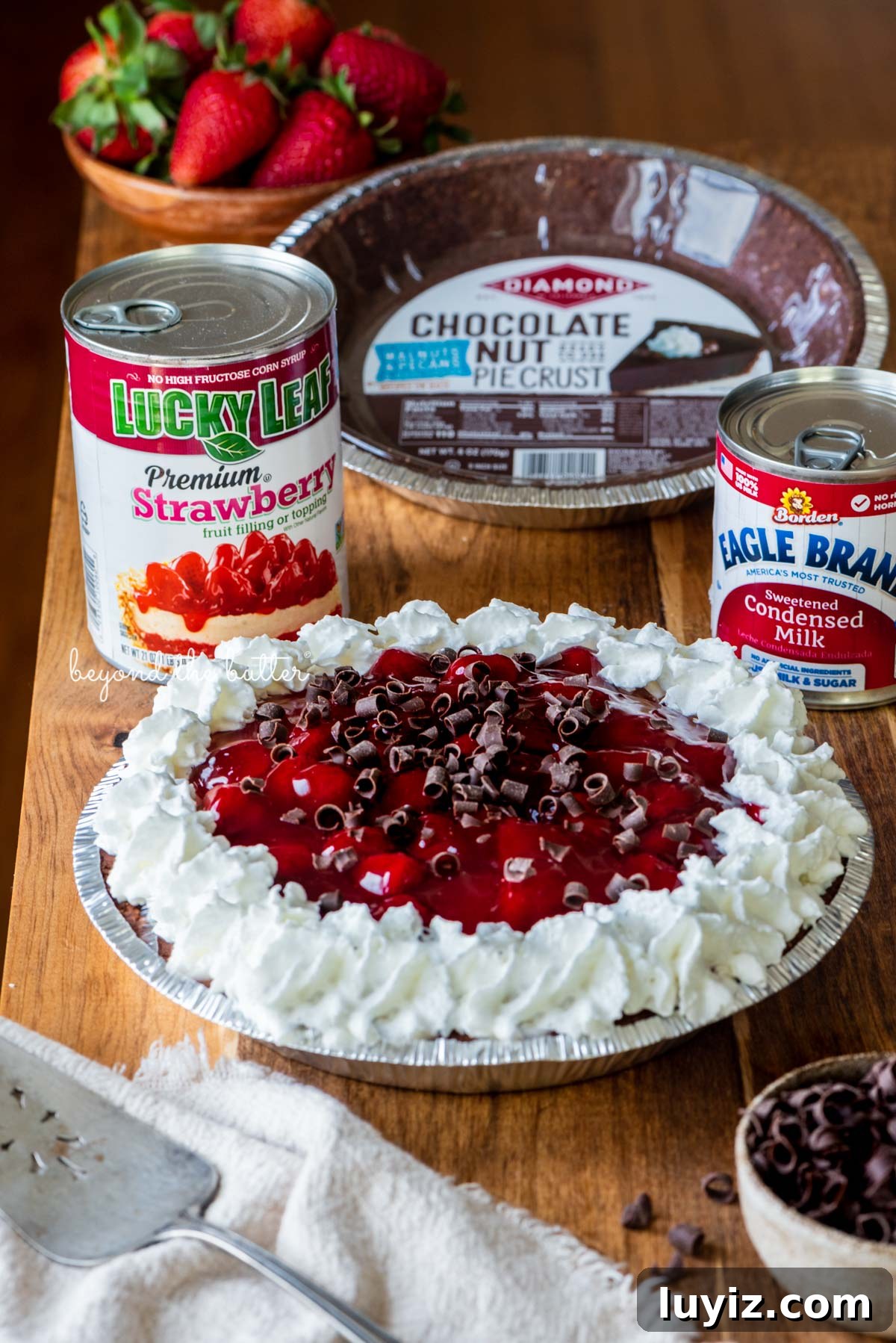 No-Bake Chocolate Strawberry Pie Recipe for Summer Parties 5 Diamond of CA® chocolate nut pie crust, Lucky Leaf® strawberry pie filling, and Eagle Brand® sweetened condensed milk with decorated no bake strawberry chocolate pie with small bowl of chocolate curls and strawberries on wood table | All images © Beyond the Butter®