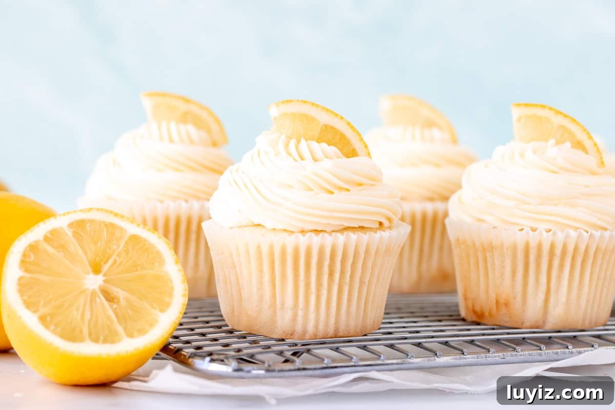 Zesty Lemon Cupcakes with Luscious Lemon Buttercream Frosting 3 Moist lemon cupcakes with frosting on wire cooling rack with half a lemon
